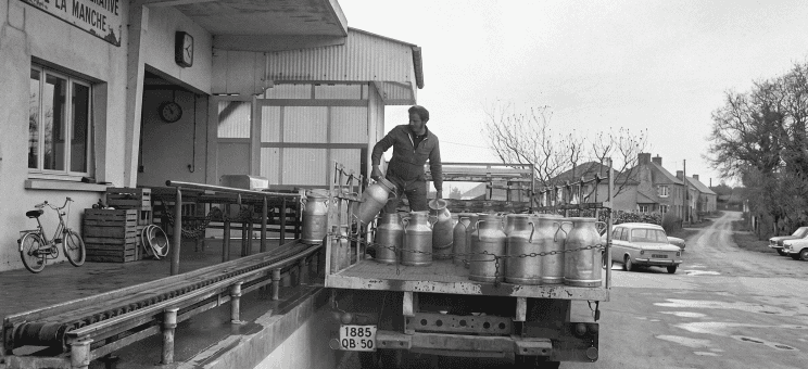 Un laitier charge des bidons de lait métalliques sur un plateau, photo des années 1960 en noir et blanc