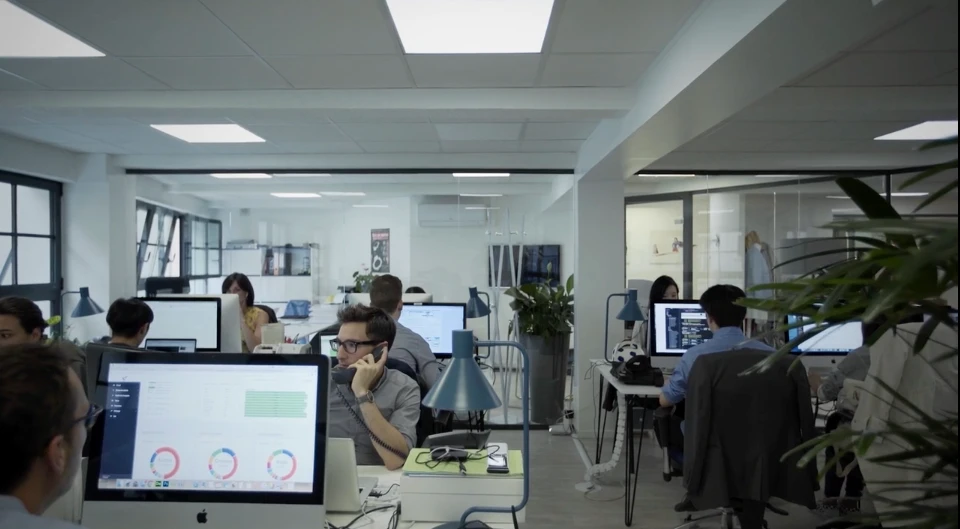 Modern red brick apartment or office building viewed from below against a blue sky, showcasing its geometric architecture with evenly spaced windows and balconies.