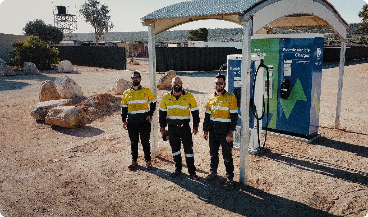 Powerhouse Renewables Group team standing by an electric vehicle fast charger in a remote Australian industrial area.
