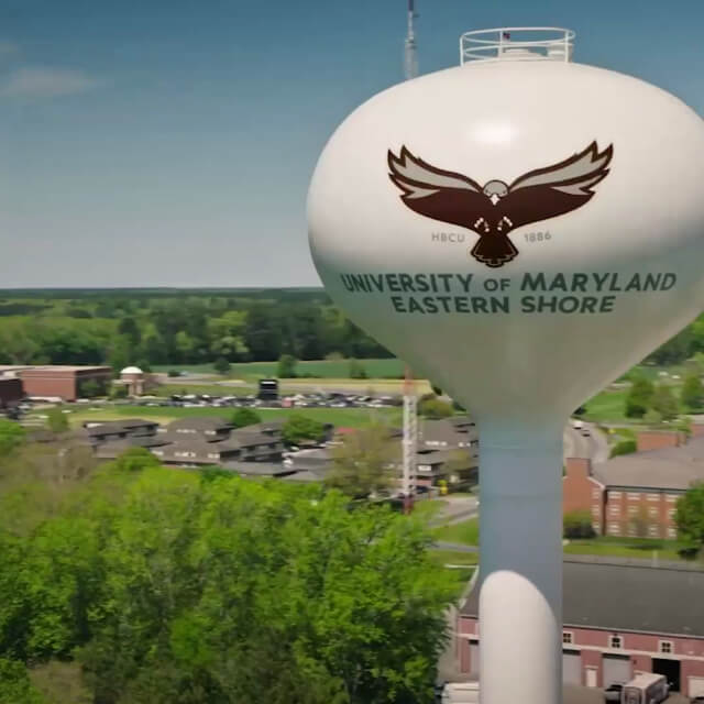White water tower with a hawk logo and the text University of Maryland Eastern Shore stands above campus buildings and greenery, reflecting a strong brand strategy recognized from Baltimore to beyond.