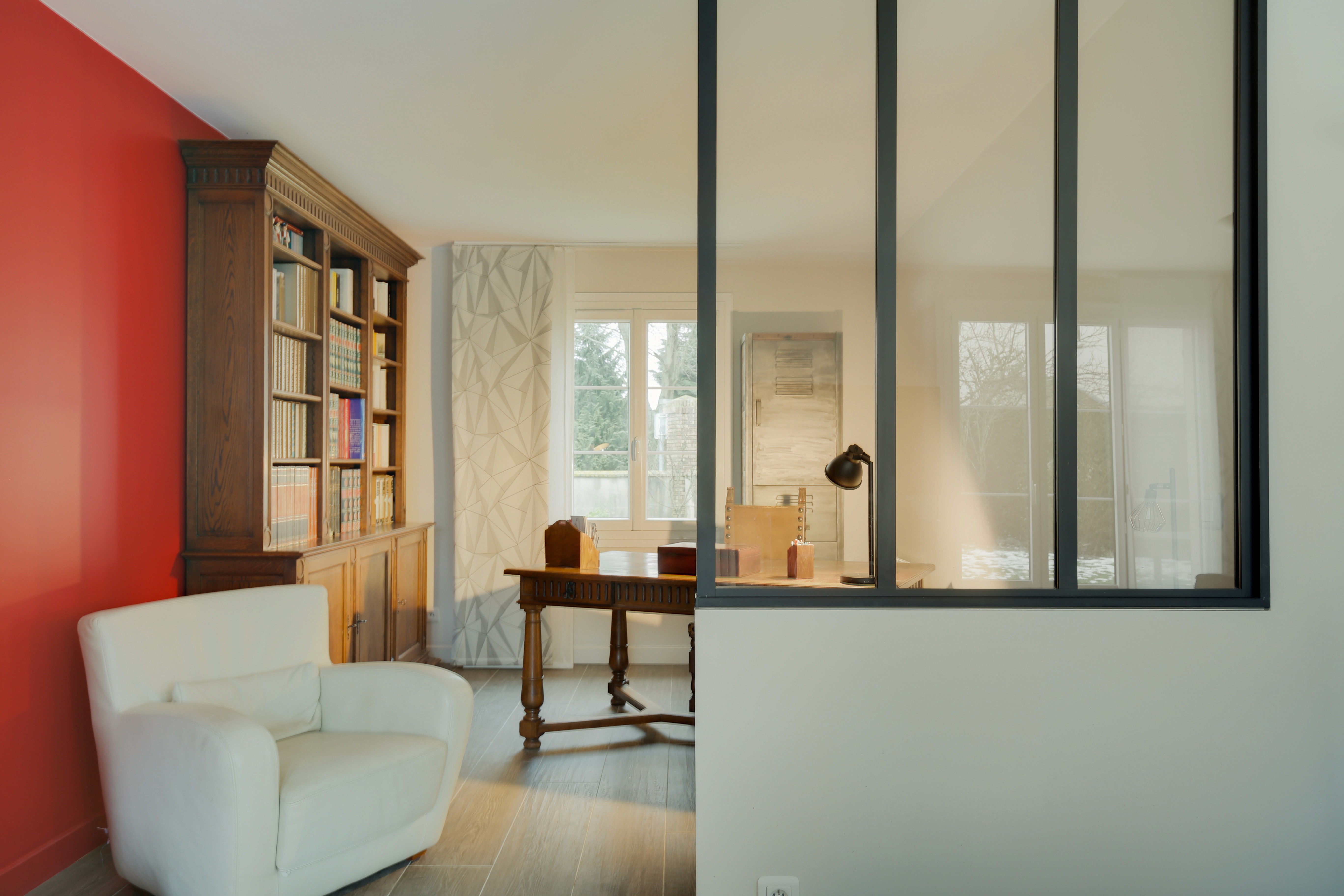 Rénovation bureau domicile Paris Est avec fauteuil blanc, bureau bois, grande bibliothèque et cloison verre séparatrice, transformation complète.