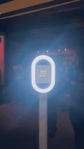 The Classic Photobooth by Studio 7 live at an event. The booth is illuminated through its ring lights with a screen saying 