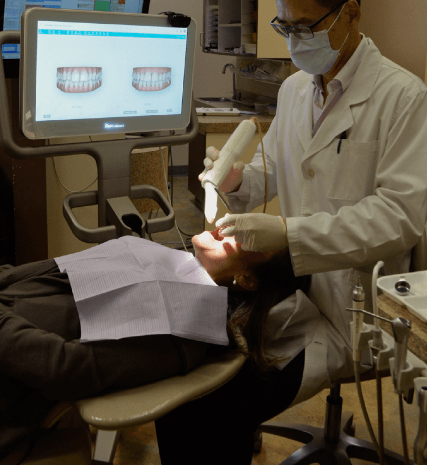 A dentist wearing a white coat and mask performing an orthodontic procedure, with a computer screen displaying dental images in the background.