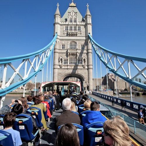 Toeristen in een open dubbeldekkerbus steken Tower Bridge in Londen over op een zonnige dag.