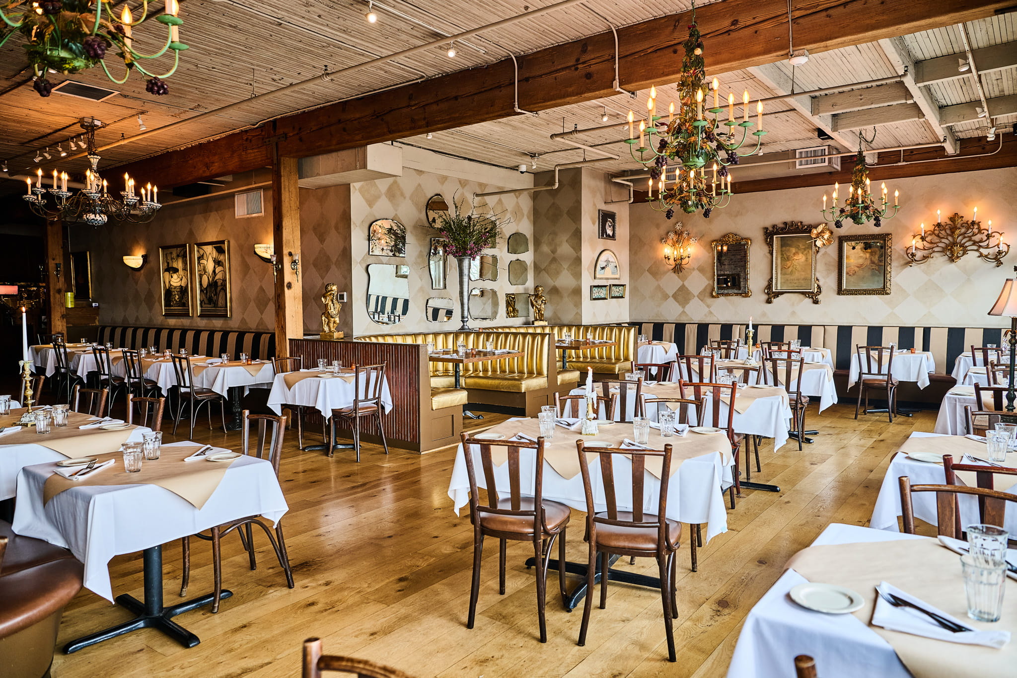 Dining room with gold tufted booths, white tablecloths, and vintage wall mirrors.