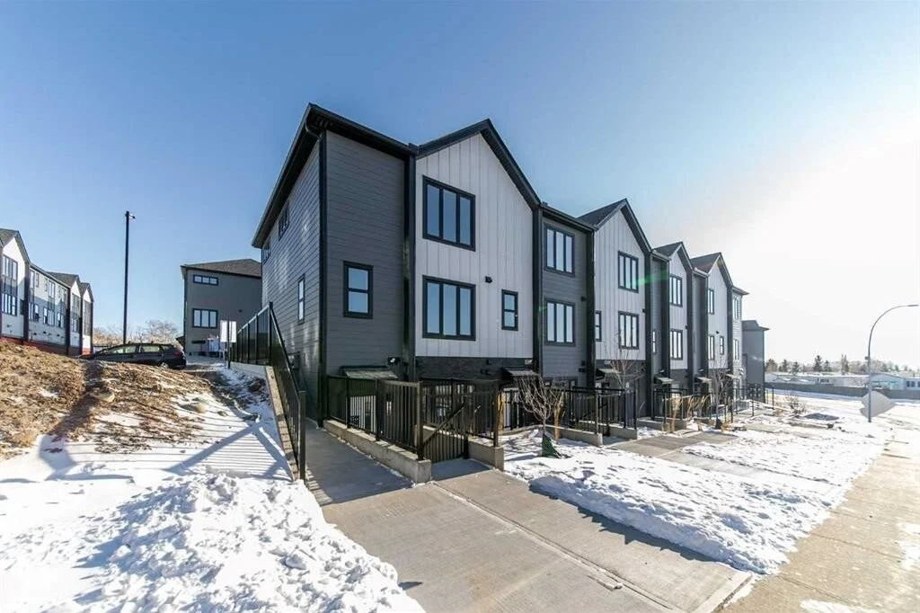 Modern charcoal and white townhouses with black railings and snow-covered sidewalks in Arbour Lake, NW Calgary