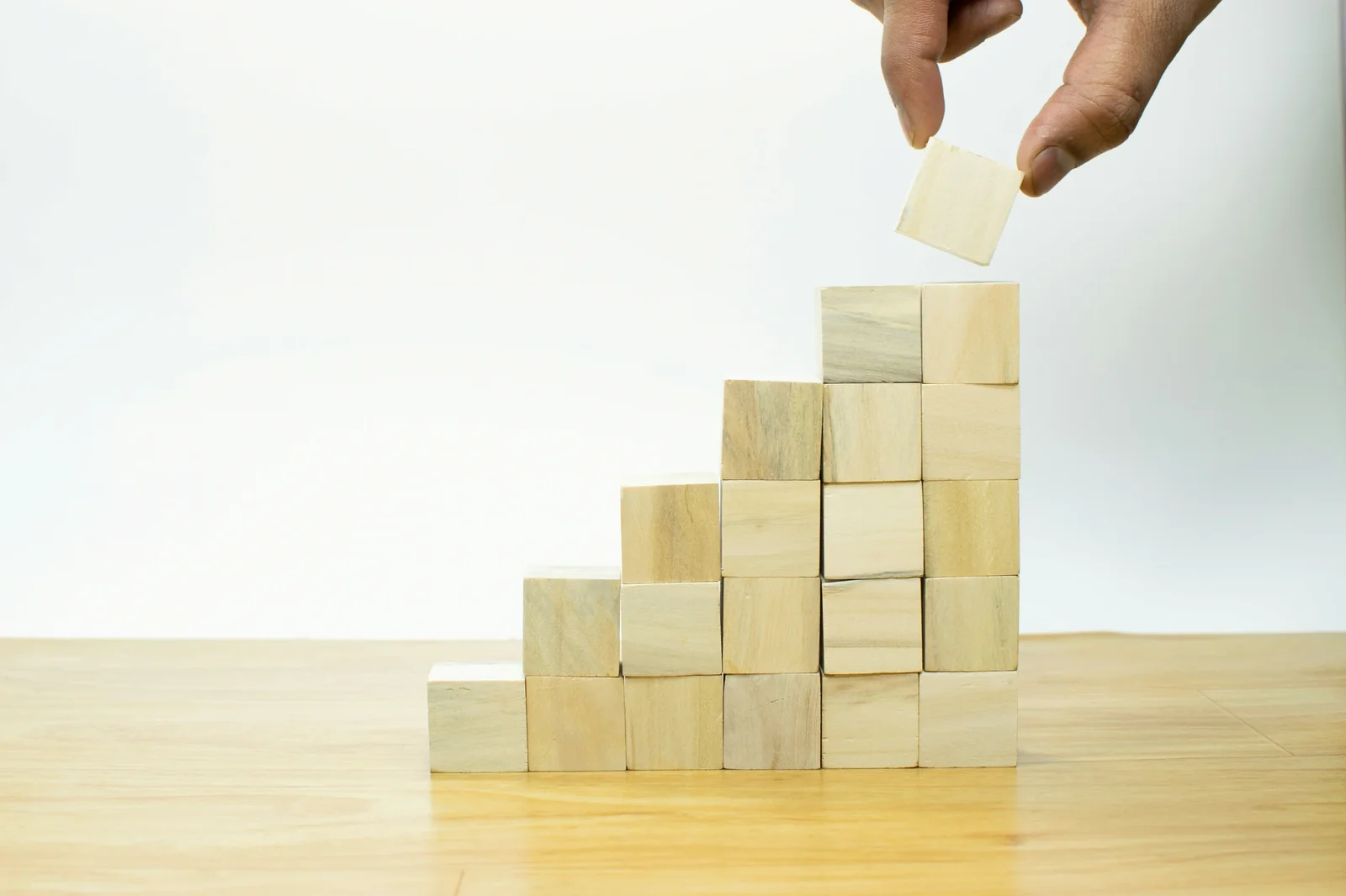 Hand placing wooden block on staircase structure, symbolizing business growth and strategic building.