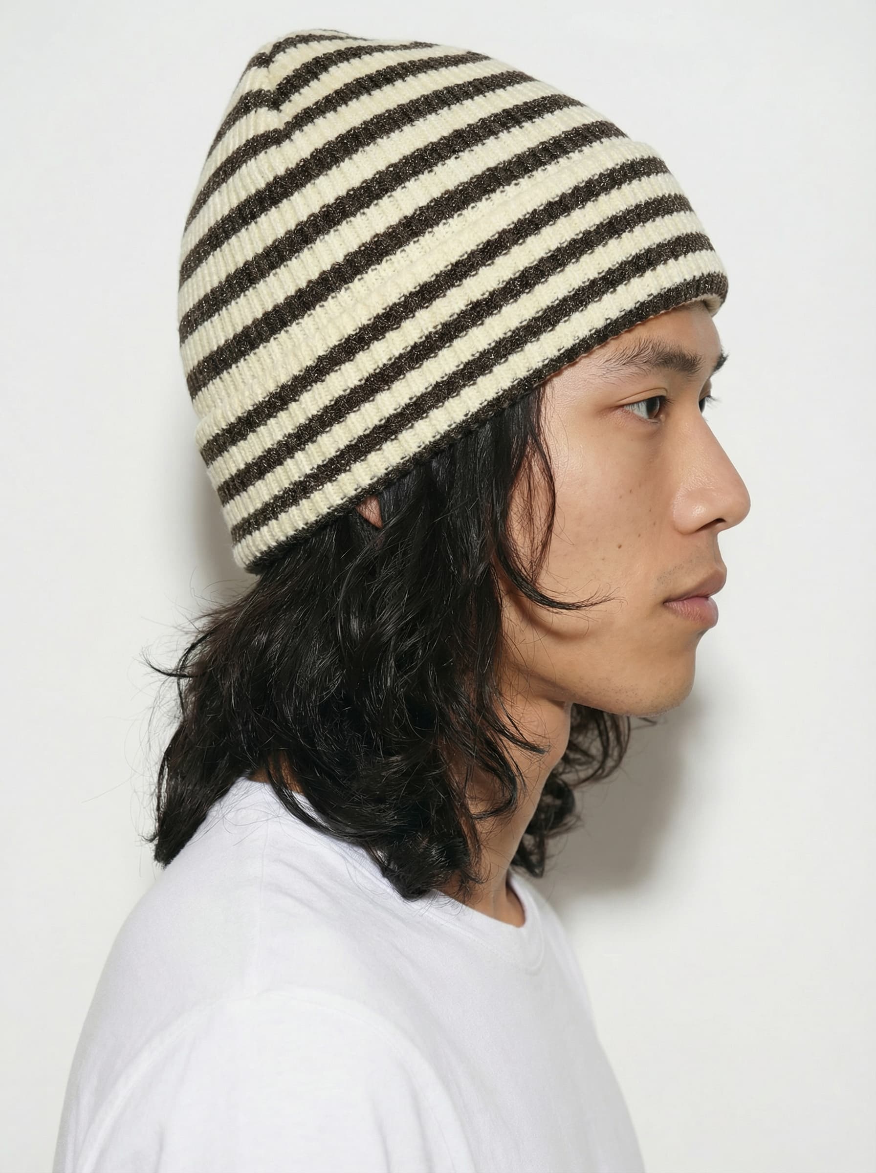 A person wearing a plain white t-shirt and a black cap stands against a neutral gray background, looking directly at the camera, with their hands relaxed by their sides.