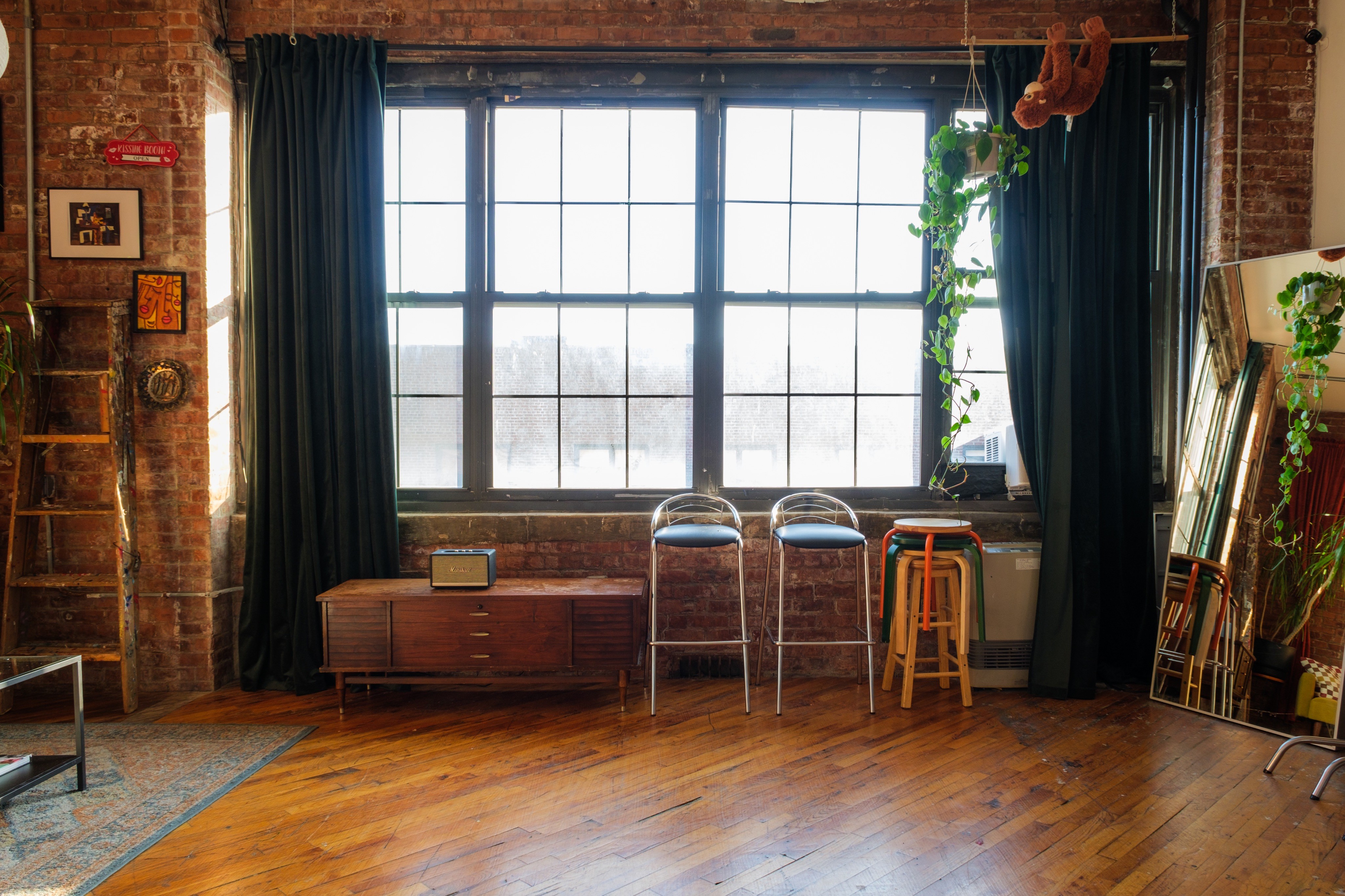 A photo studio wall adorned with a large, vibrant floral installation, creating a striking backdrop. The room also features hardwood floors, a chalkboard-style door decorated with doodles, and a setup for background rolls.