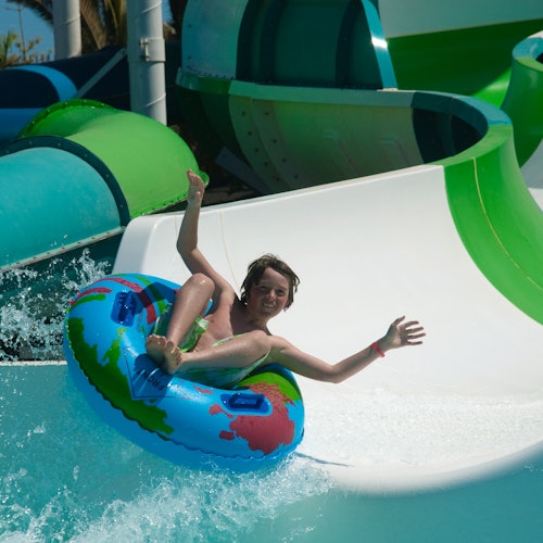 一个人在色彩斑斓的充气轮胎上开心地滑下水滑梯，脸上充满欢乐，并双手高举。