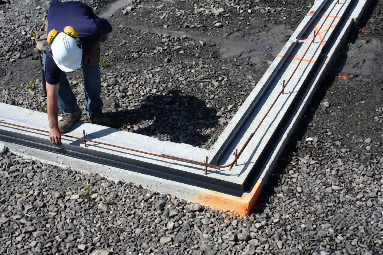 A man setting the base angle of the concrete corner of a new home foundation