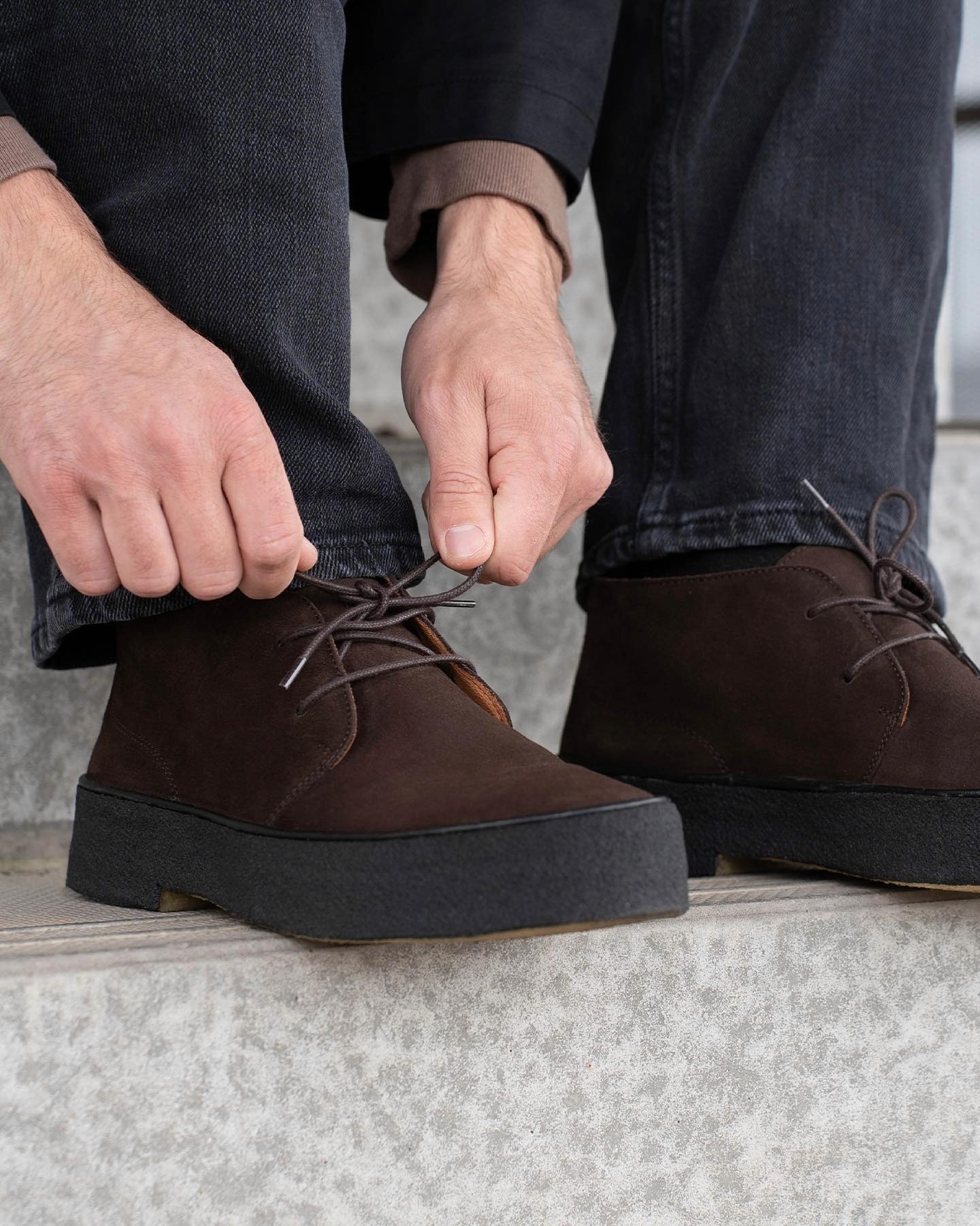 Un homme fait les lacets de ses chaussures, des chukka playboy comme en porte Steve McQueen dans Bullit