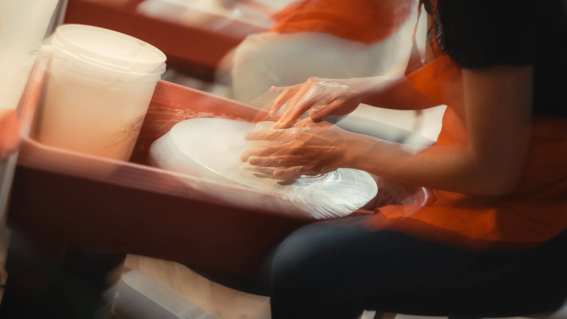 Motion-blurred hands centering clay on a spinning pottery wheel