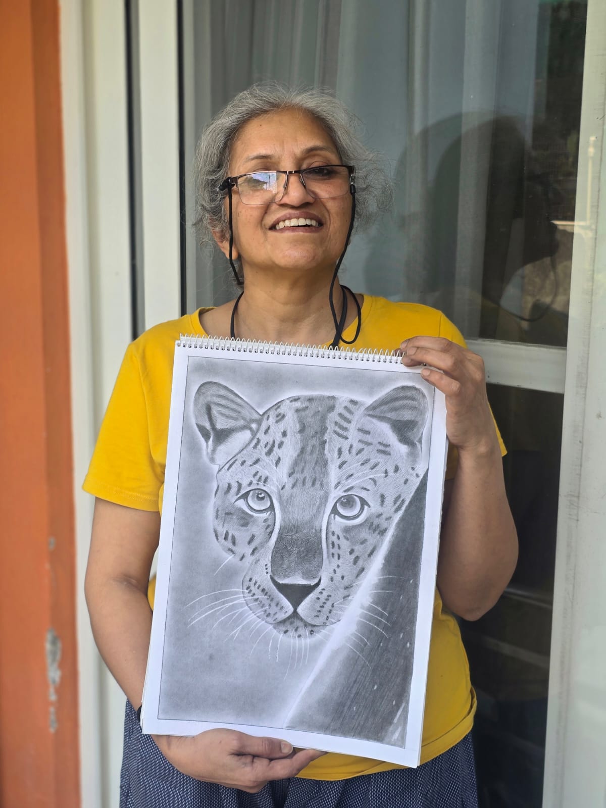 Creative Pod student holding a pencil sketch of a cheetah on the balcony of The Creative Pod studio.
