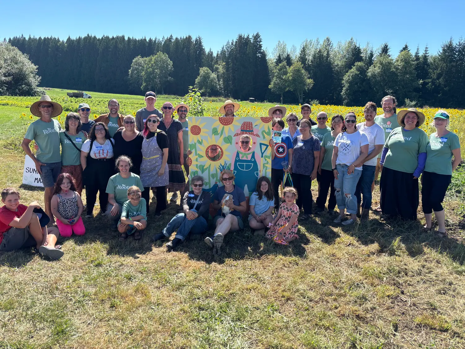 Large group of adults and children gathered together outdoors in a grassy field.