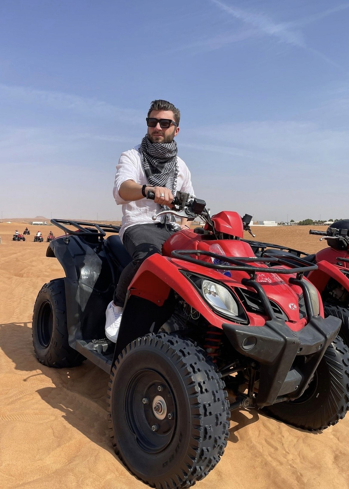 Guest jumping beside a black Can-Am Maverick X3 dune buggy in the Dubai desert during a Dune Quest Tours adventure experience