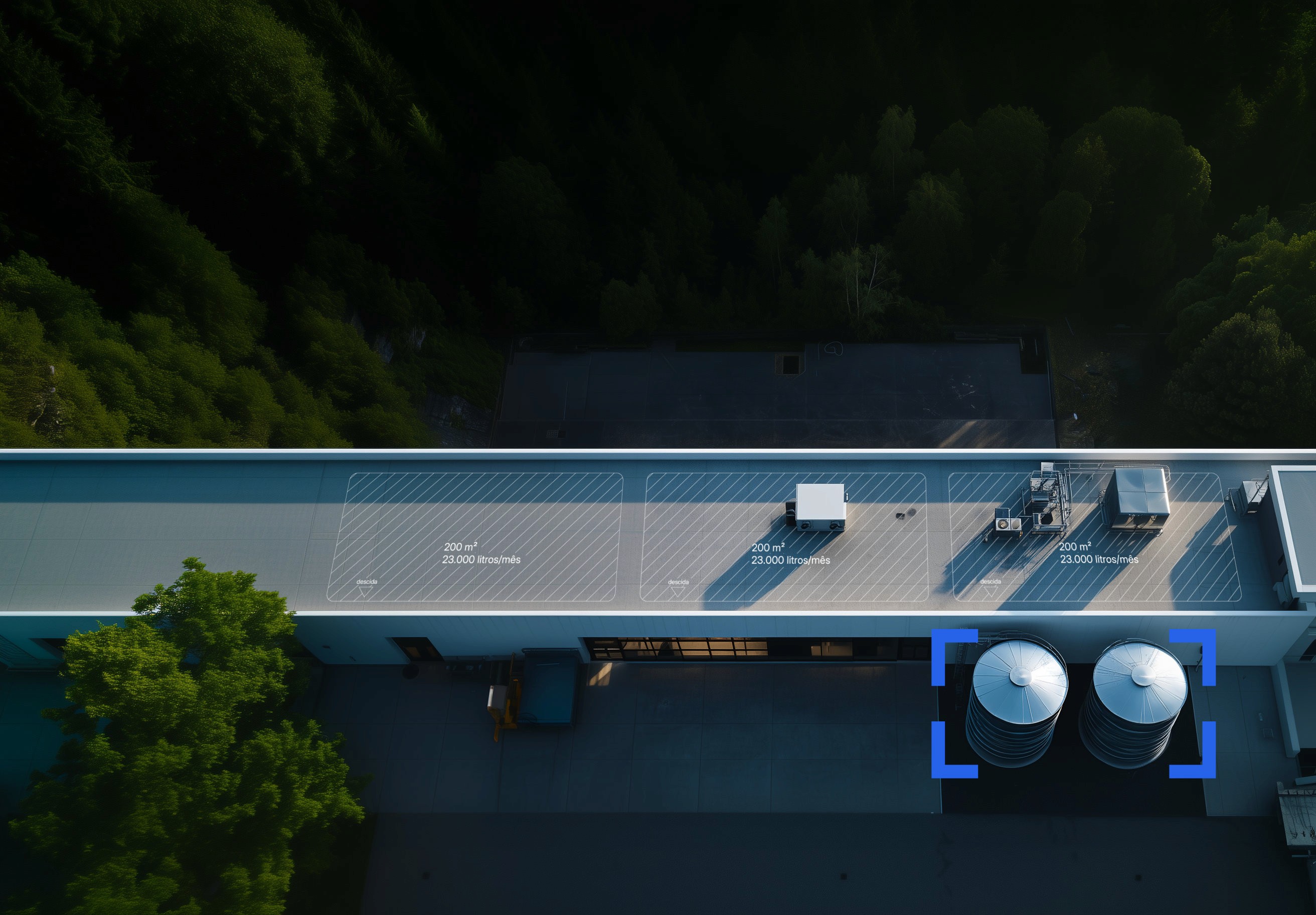 vista aérea do telhado de um edifício industrial com dois grandes reservatórios de água da chuva adossados ao exterior e, ao fundo, um bosque