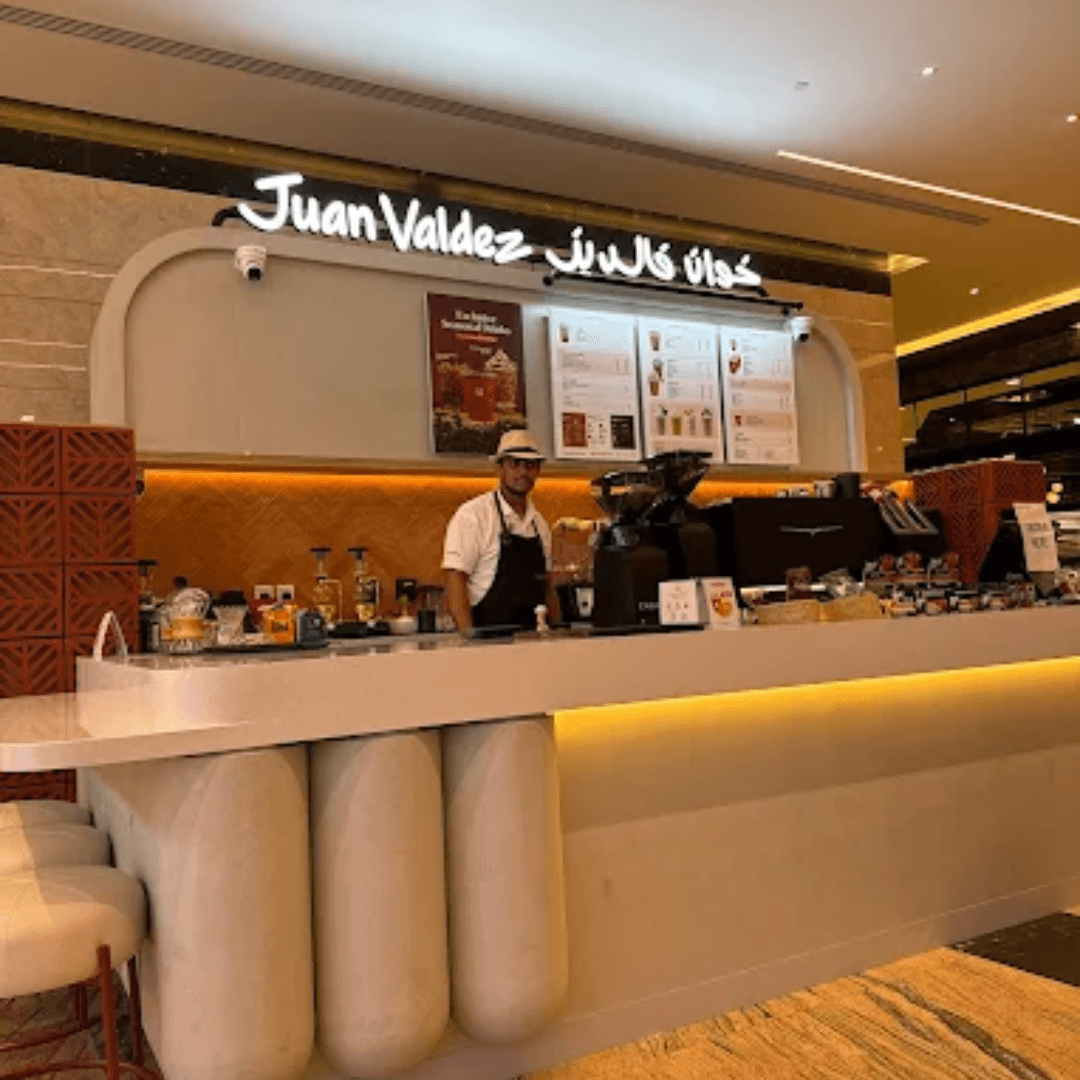 Modern cafe counter with glowing lights and a barista preparing coffee at Juan Valdez Café in Abu Dhabi.