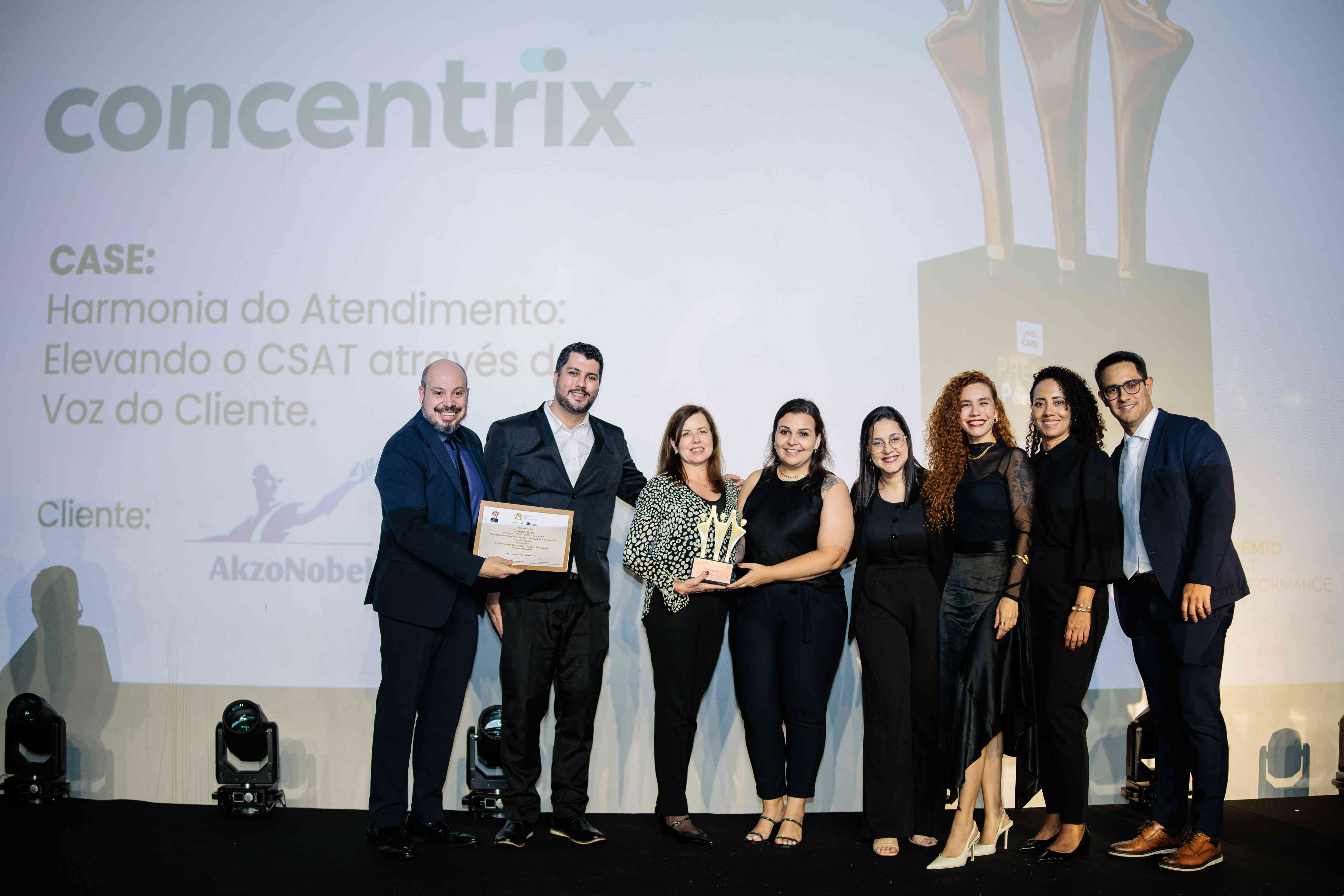 Executivos da Concentrix posando com troféu bronze e certificado no palco do Prêmio Best Performance 2025