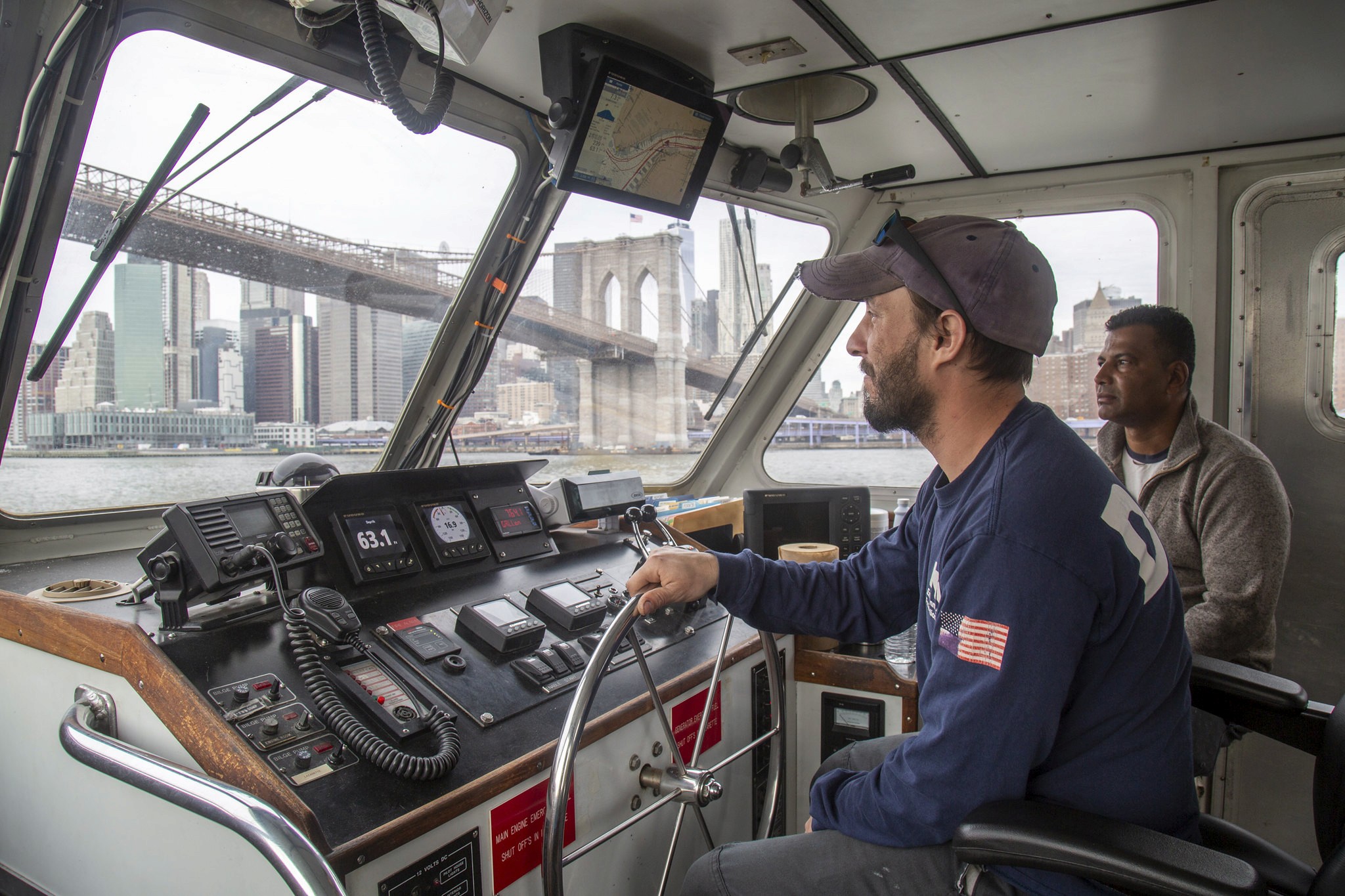 NYC DEP employees steering a boat down the East River under the Brooklyn Bridge