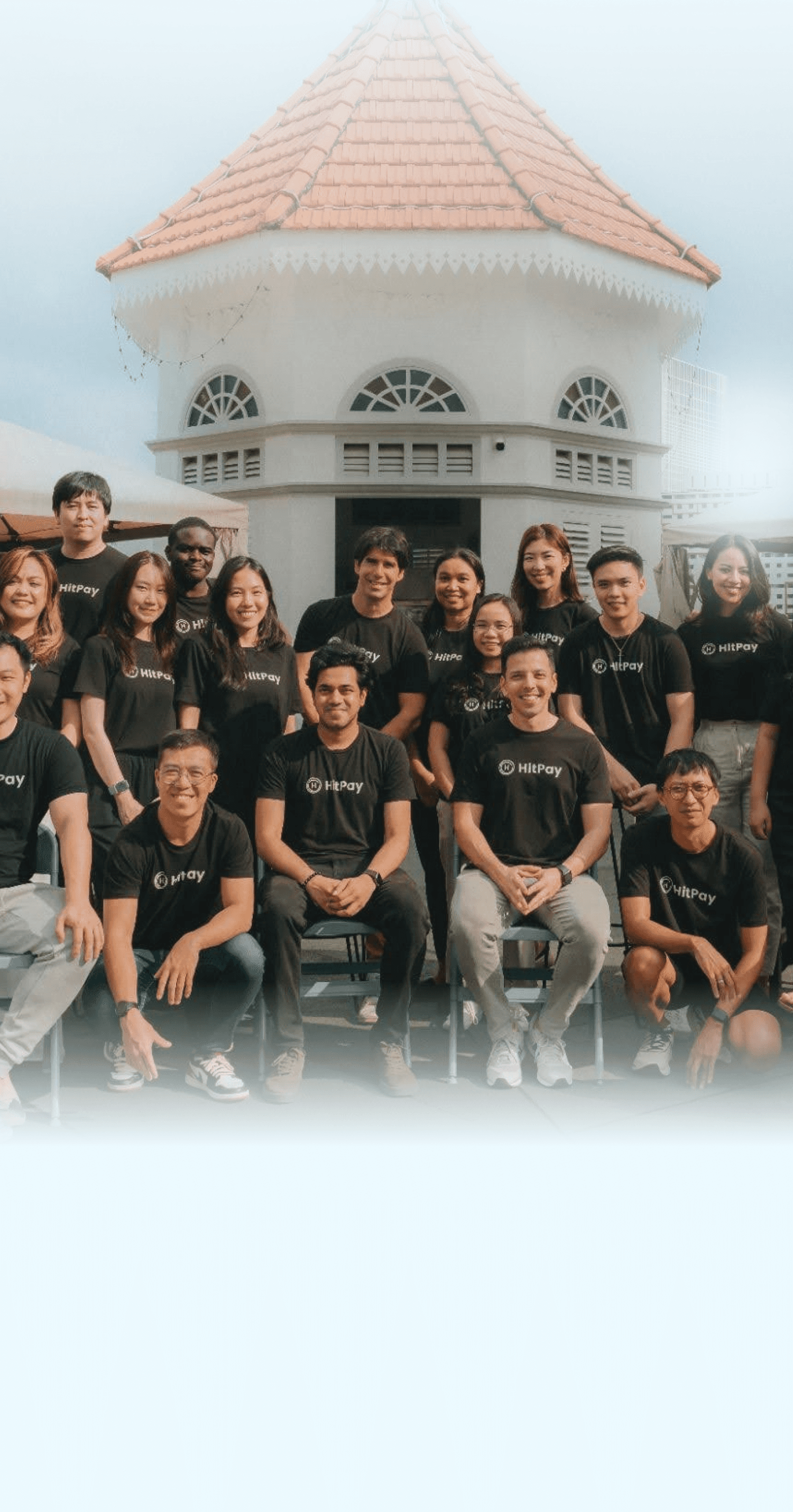 Diverse team in black shirts with 'HitPay' logo, posing outdoors. Everyone is smiling.