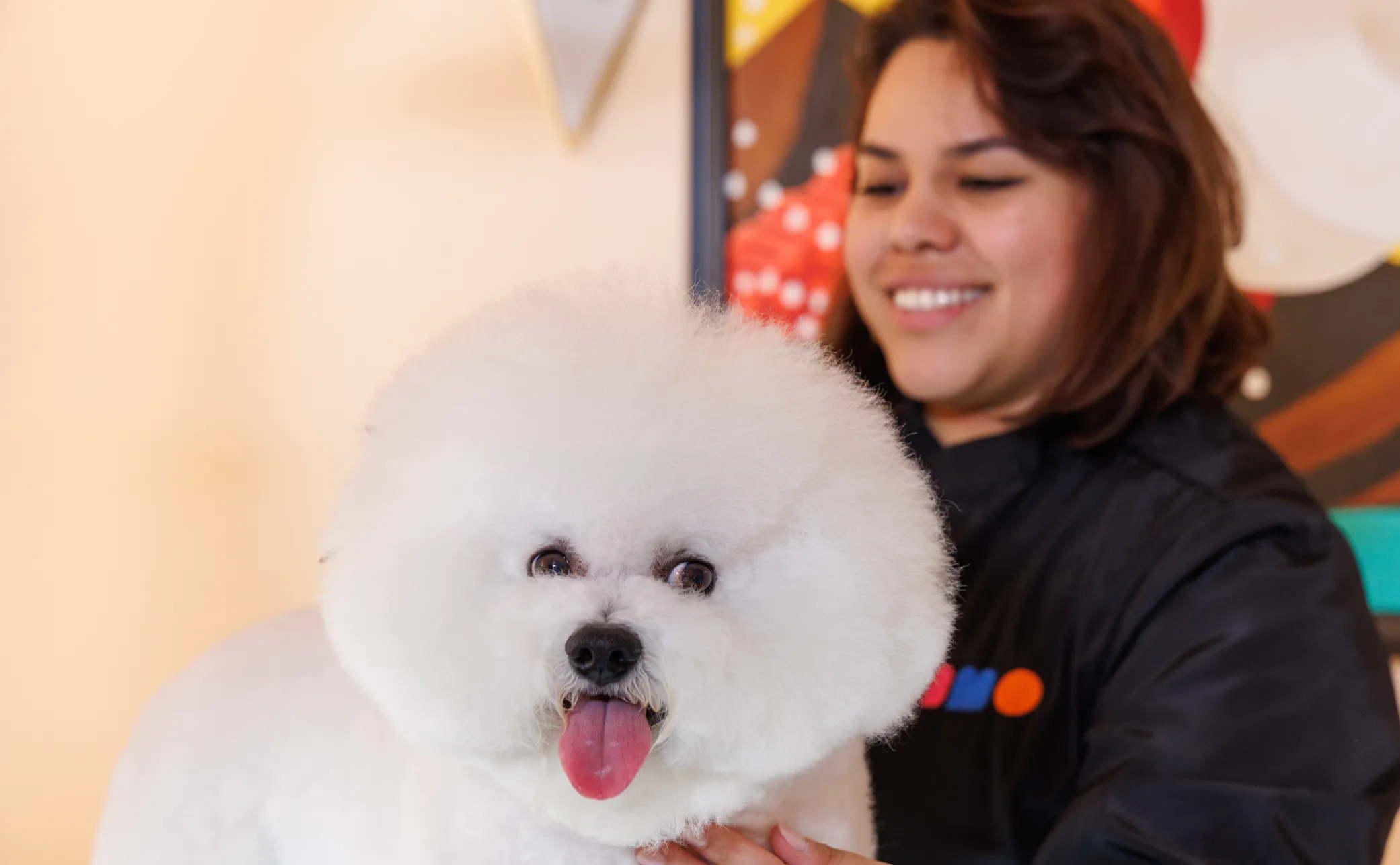 Smiling groomer holding a fluffy white dog at MIMO University Heights.