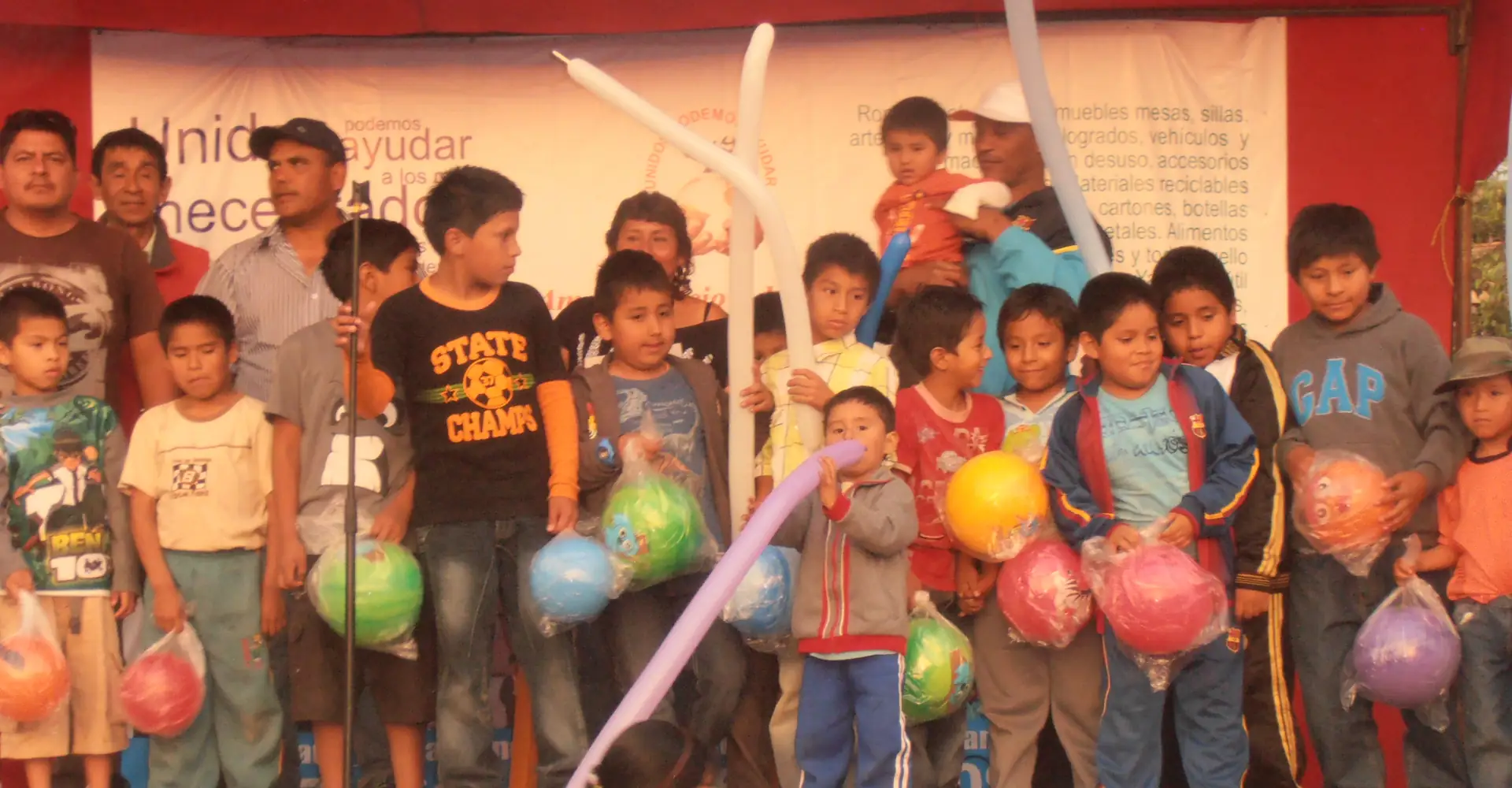 Grupo de niños y adultos felices sosteniendo pelotas y globos de colores.