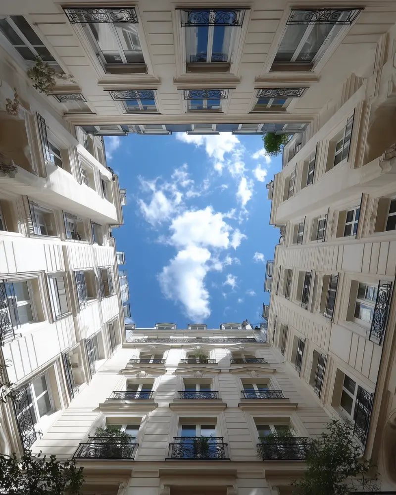 Cour intérieure d’un immeuble parisien vue vers le ciel avec architecture élégante.