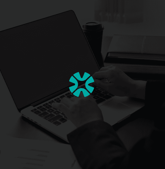 A smiling young man with crossed arms, wearing a plaid shirt and white t-shirt, poses against a dark background.