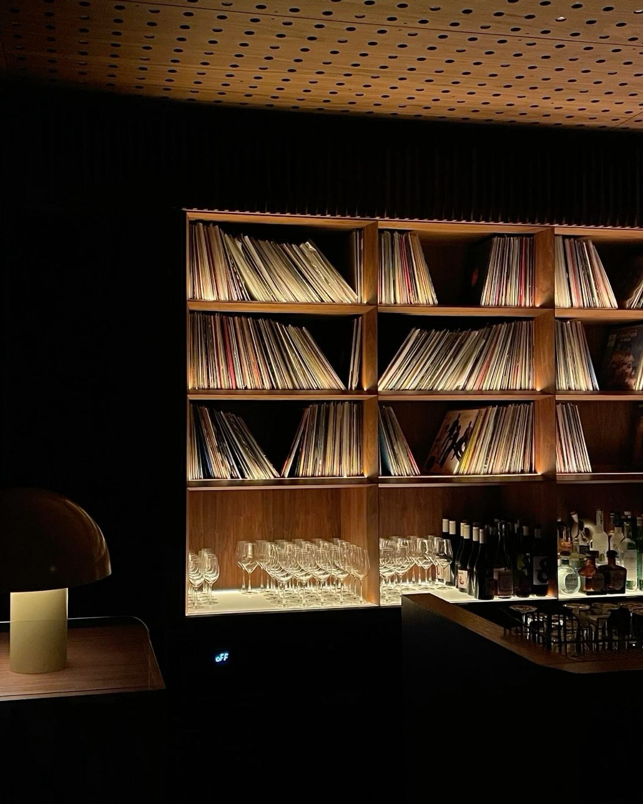 Dark listening bar with record shelves, large speakers, audio equipment, and a stone counter.