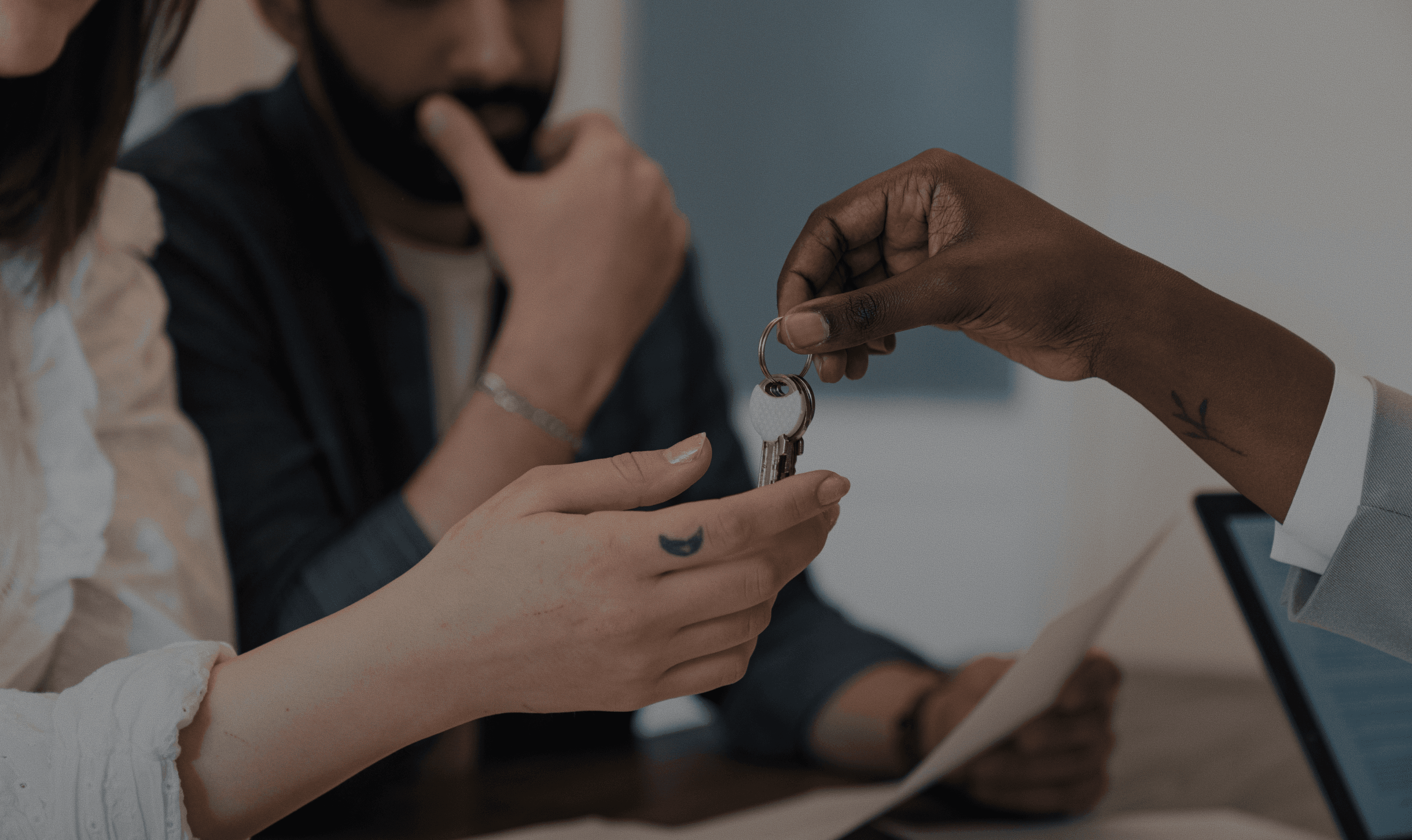 A real estate agent hands over keys to a couple sitting at a desk, symbolizing successful home buying and potential open rate improvement.