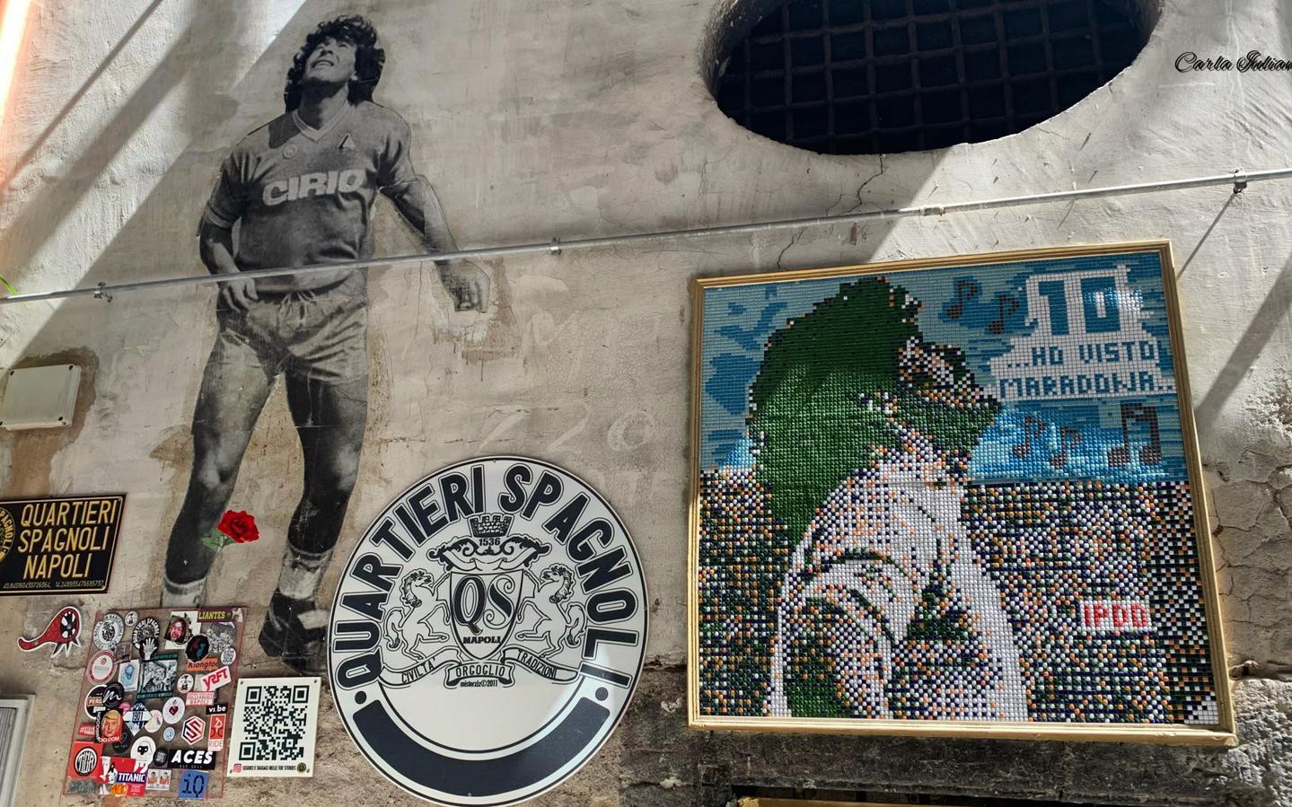 在那不勒斯西班牙区的迭戈·马拉多纳壁画，周围是马赛克艺术和当地街头标志。