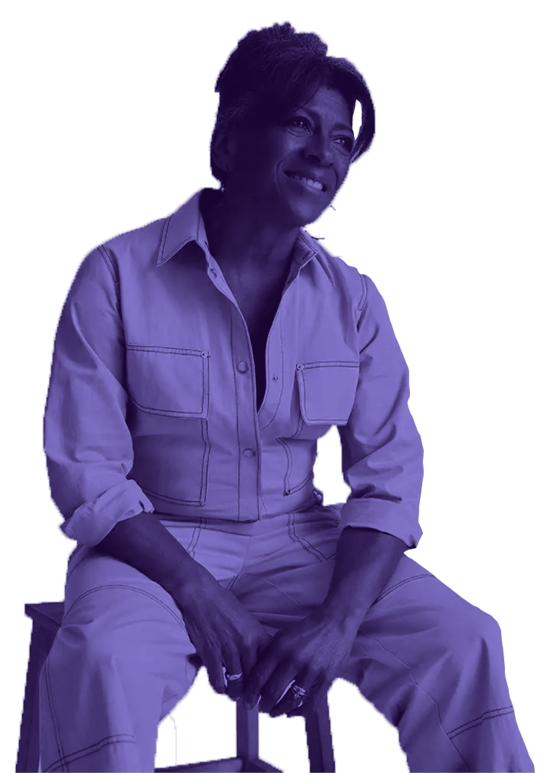 A woman seated on a stool, dressed in a stylish jumpsuit, exuding a relaxed and confident demeanor.