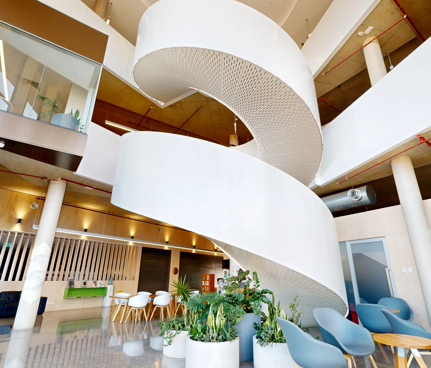 A dramatic upward view of a modern white spiral staircase spanning multiple levels inside the Stretton Centre commercial facility, featuring polished concrete floors and indoor plants. Captured as an enterprise-grade 3D digital twin by ABM visual.
