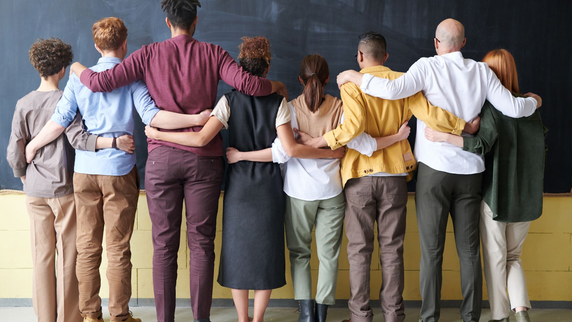 Five colleagues stand arm in arm, seen from behind