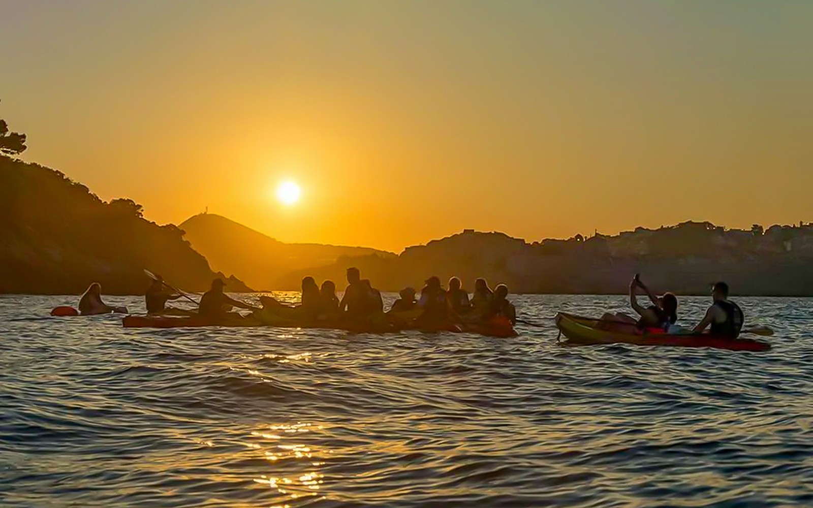 Kayakers paddling at sunset near Dubrovnik coastline.