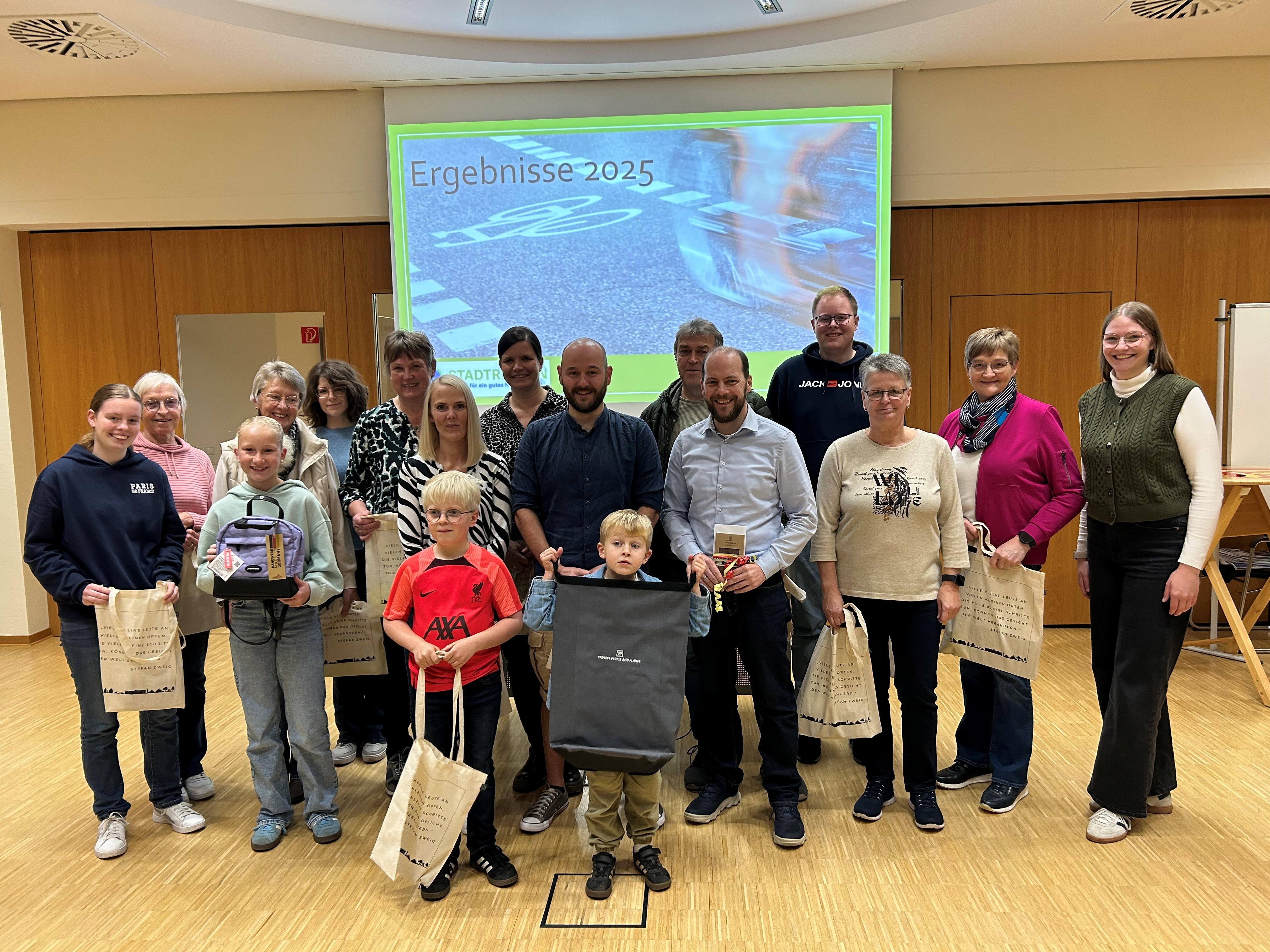 Gruppenfoto von Menschen mit einem Präsentationsbrett, auf dem „Ergebnisse 2025“ steht. Personen, die Taschen halten und für ein Foto posieren.