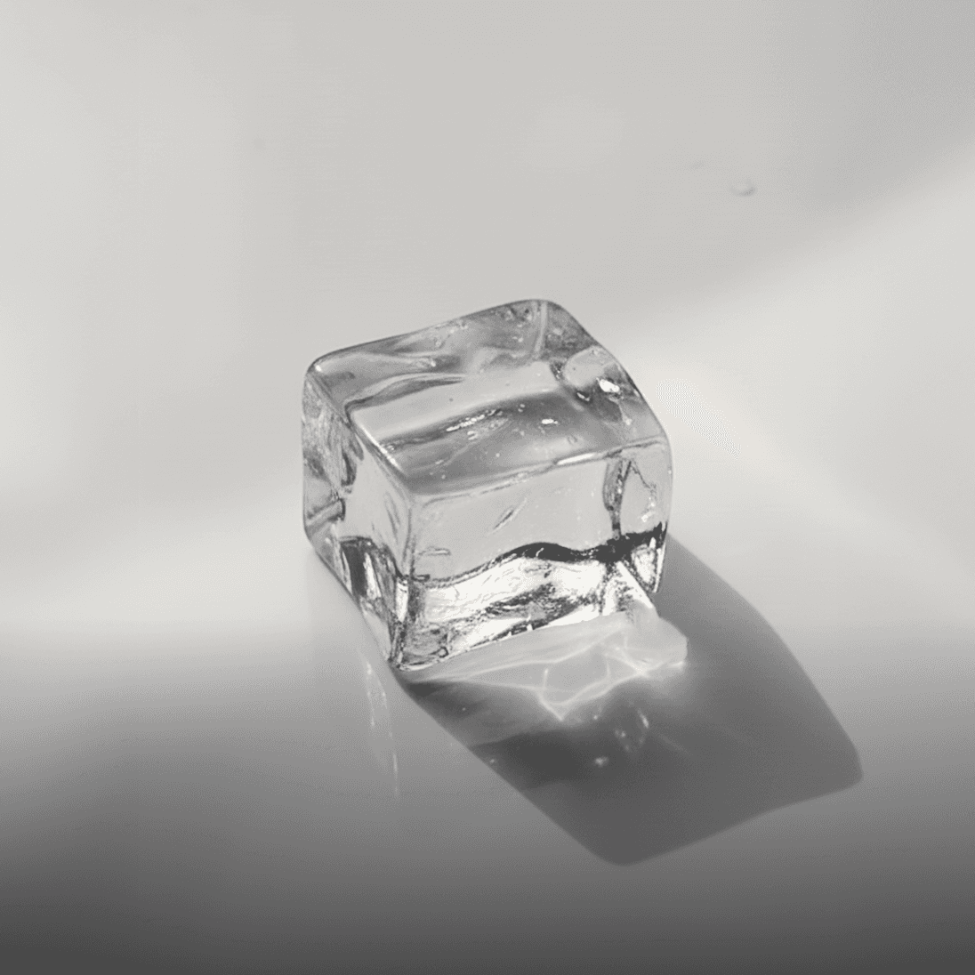 A single ice cube mid-melt on a pale surface — a small system transforming faster than it looks.