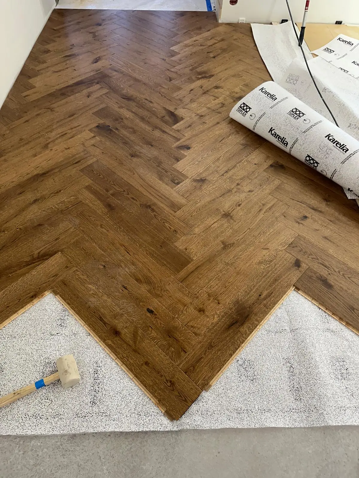 Puoliksi asennettu vaalea tammi­parketti modernissa huoneessa. Kuvassa näkyy valmis osa parkettia ja paljas betonipohja ennen asennuksen viimeistelyä.