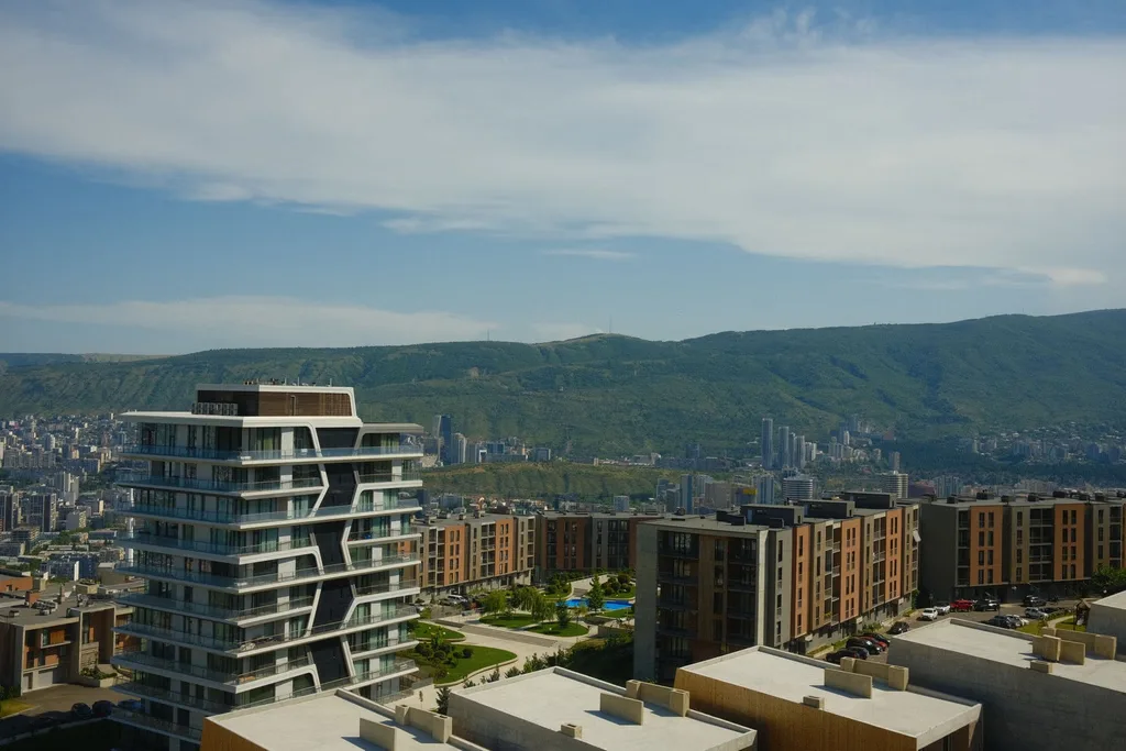Modern skyline view with green hills and high-rise buildings under a blue sky.