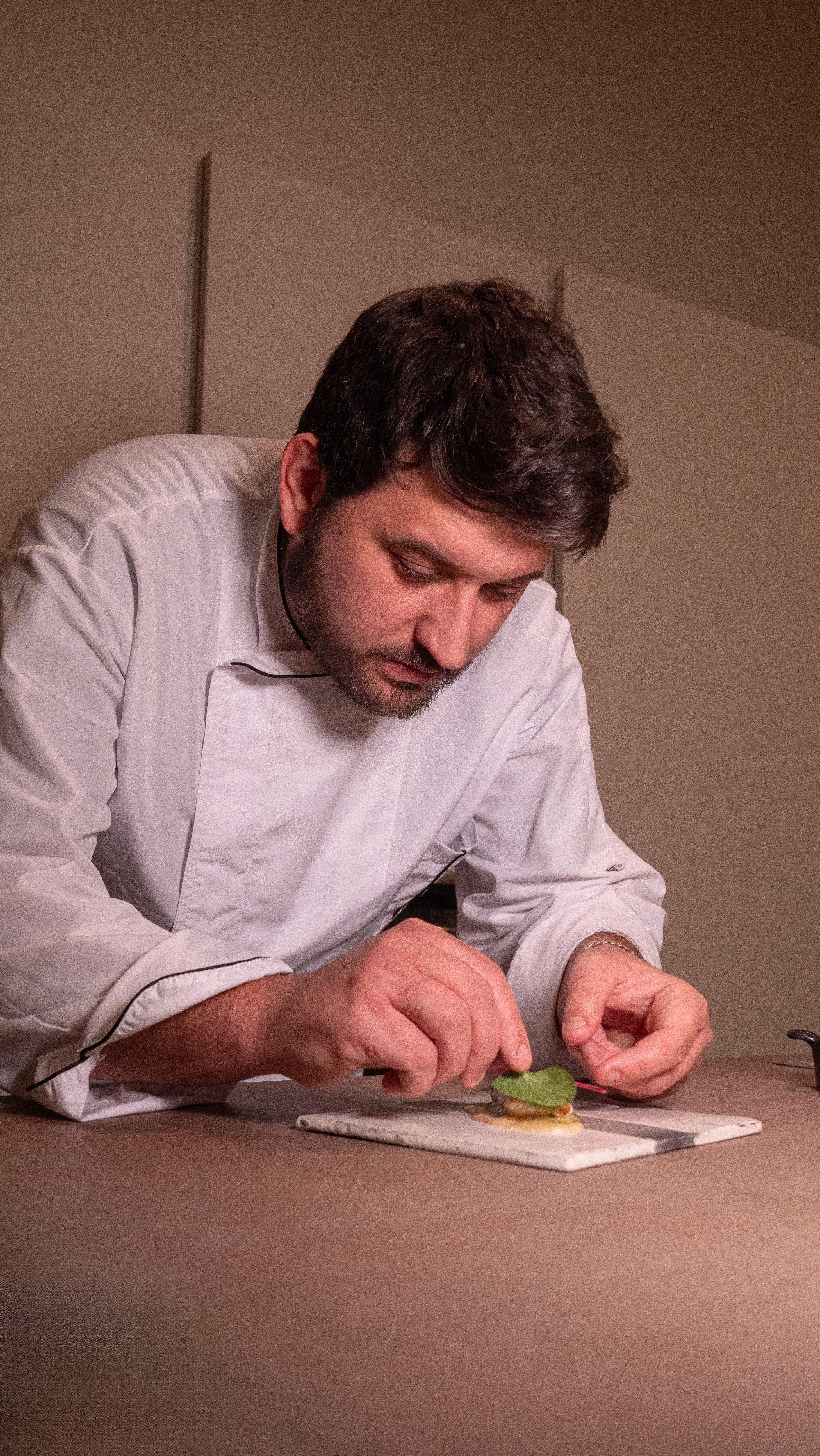 Person wearing a beige apron whisking green matcha tea in a ceramic bowl on a kitchen counter.