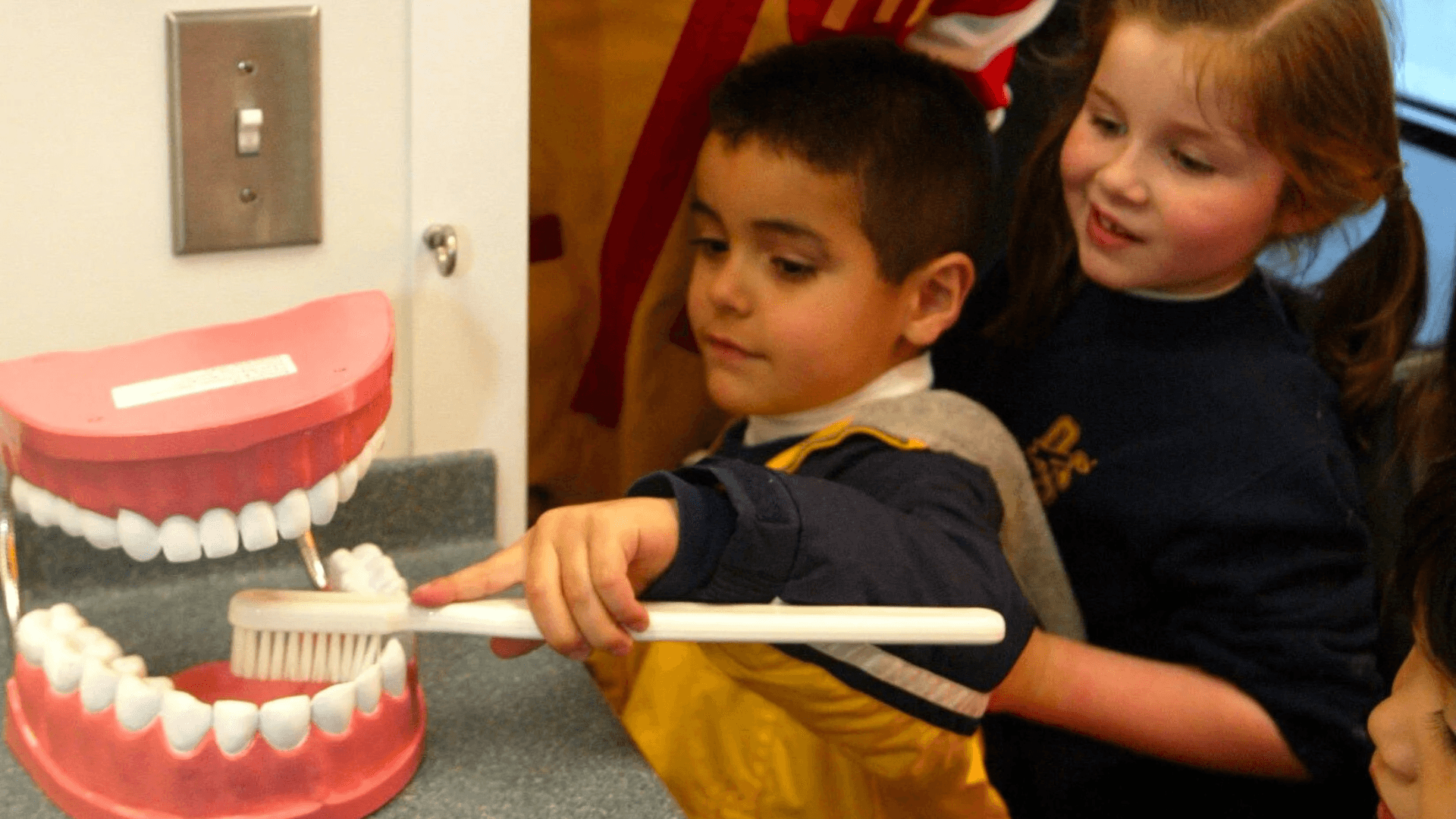 Two children practicing brushing on a large model of teeth with an oversized toothbrush