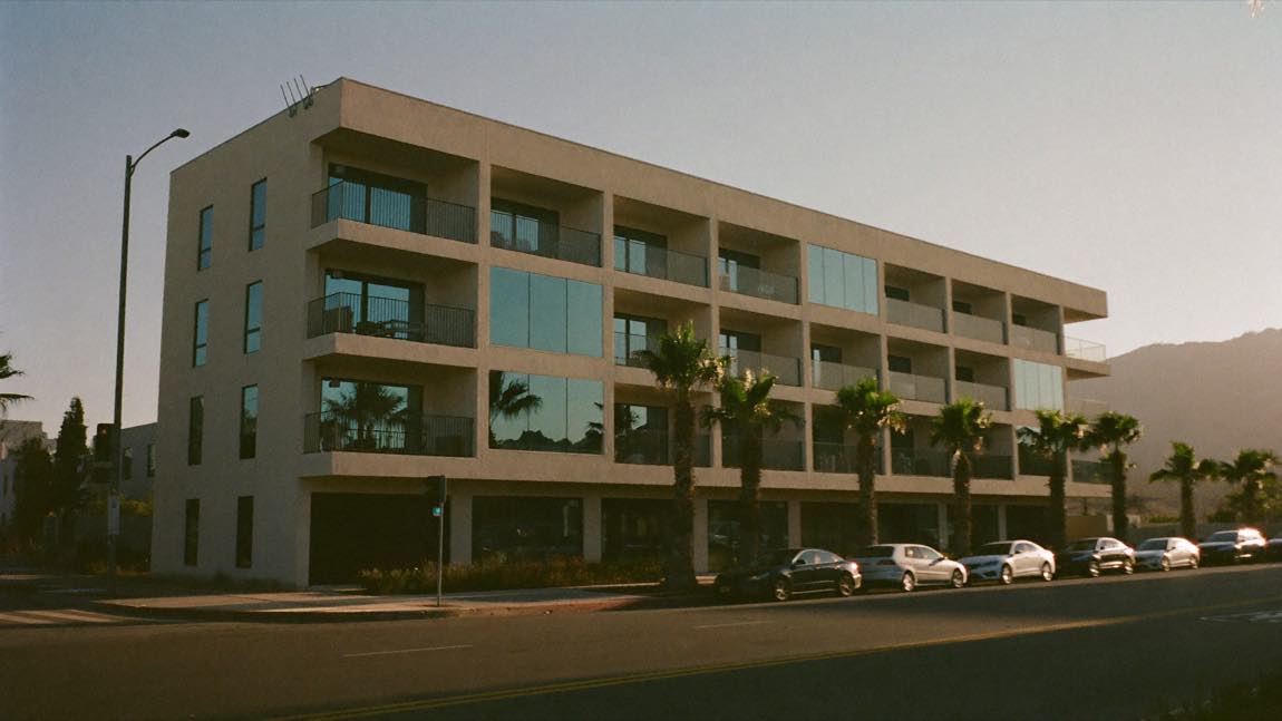 New multifamily apartment building on a palm-lined Los Angeles street at golden hour