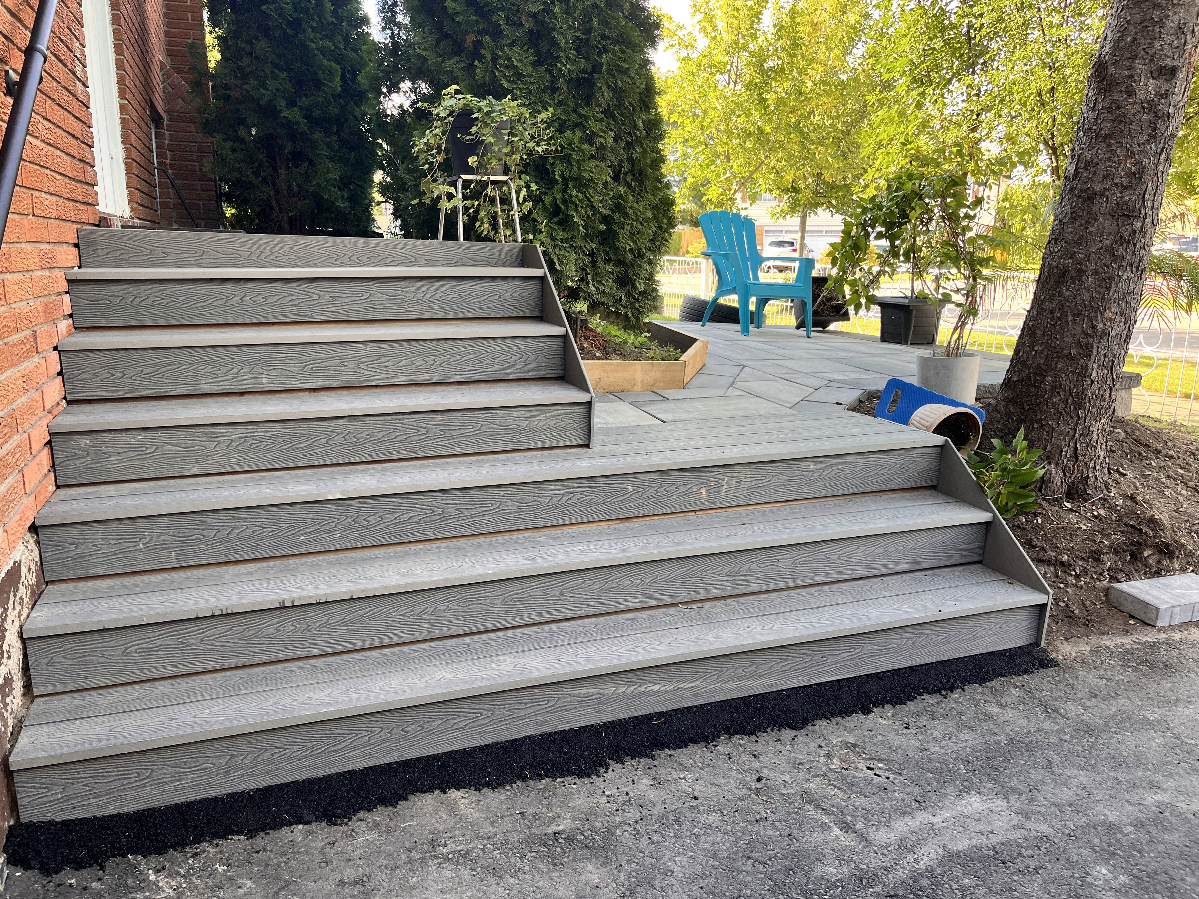 Concrete steps lead up to a brick building, surrounded by trees and grassy areas, with seating in the background.