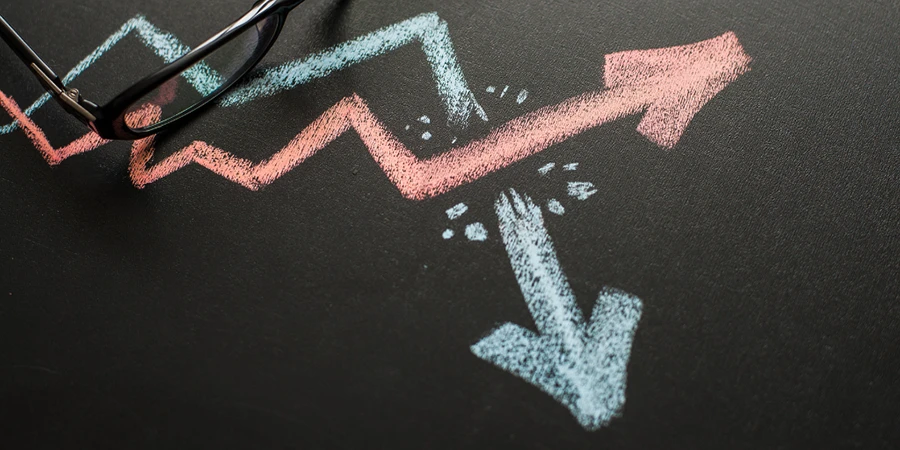 Chalk drawing of upward and downward arrows on a blackboard symbolizing growth and decline, with glasses placed nearby.