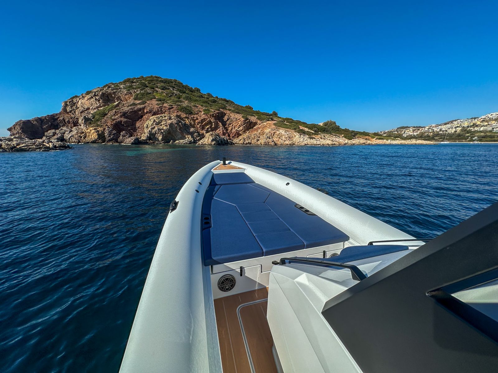 White Rock 36 speedboat with captain at helm cruising calm blue waters near Paros coastline with hills in background.