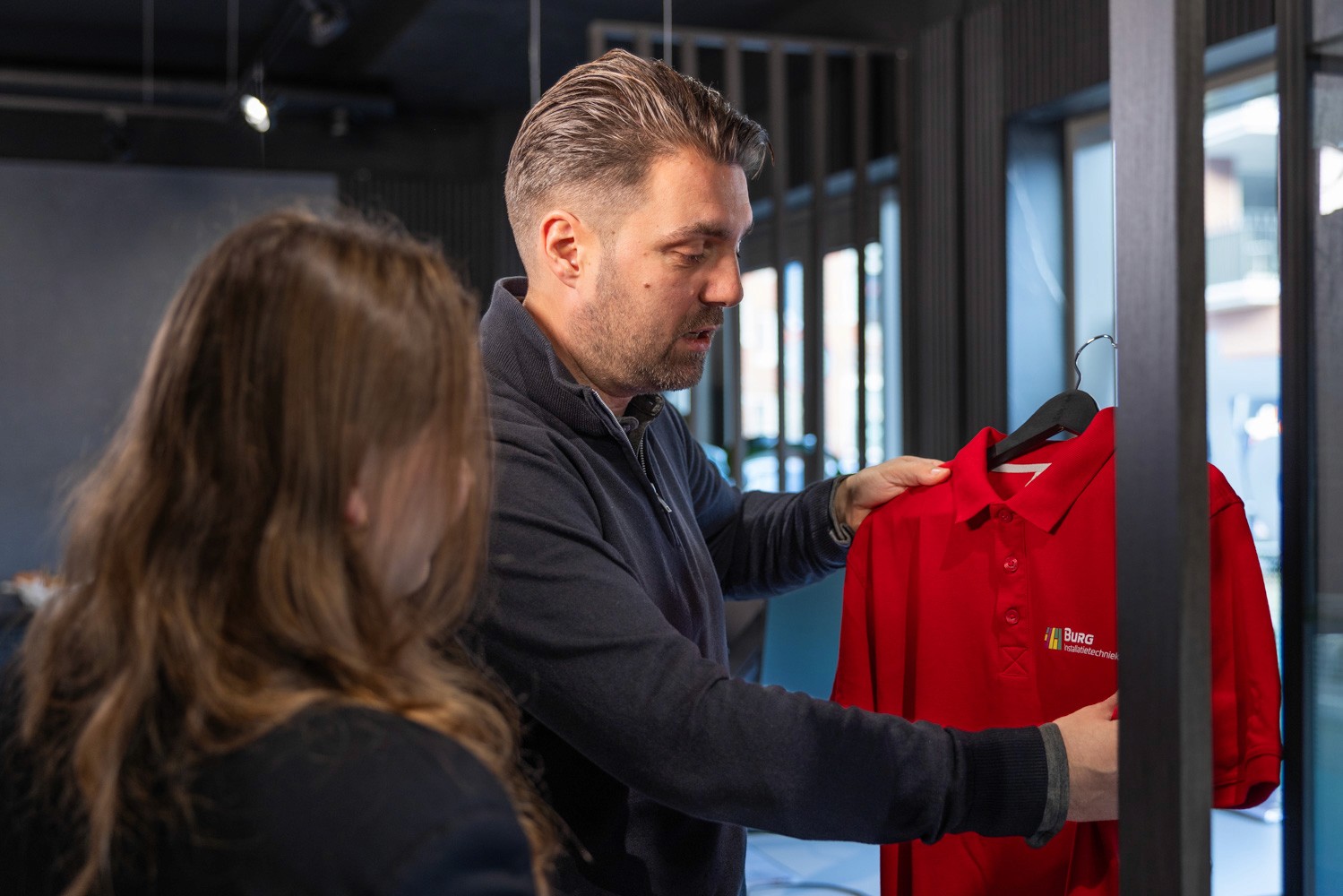 Three people in conversation with warm lighting, including a person wearing a hat and another person wrapped in what appears to be a textured shawl or sweater.