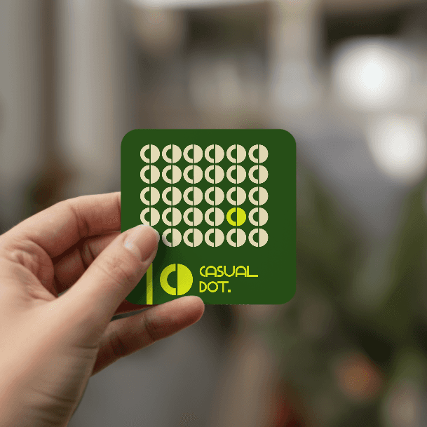 Person holding a green business card for "Casual Dot" with a pattern of white and yellow circles.