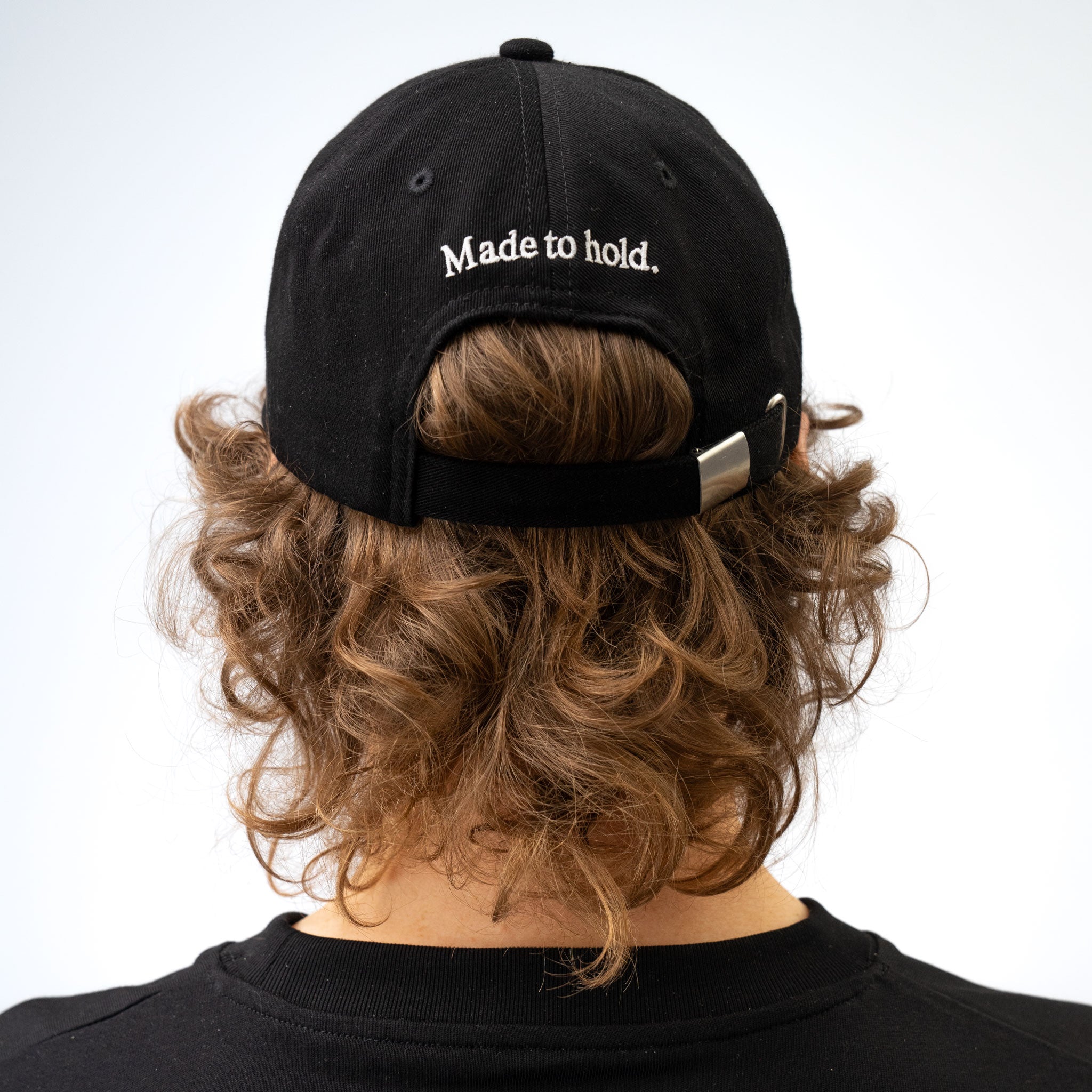 Person wearing a black cap with 'Made to hold' text on a plain background