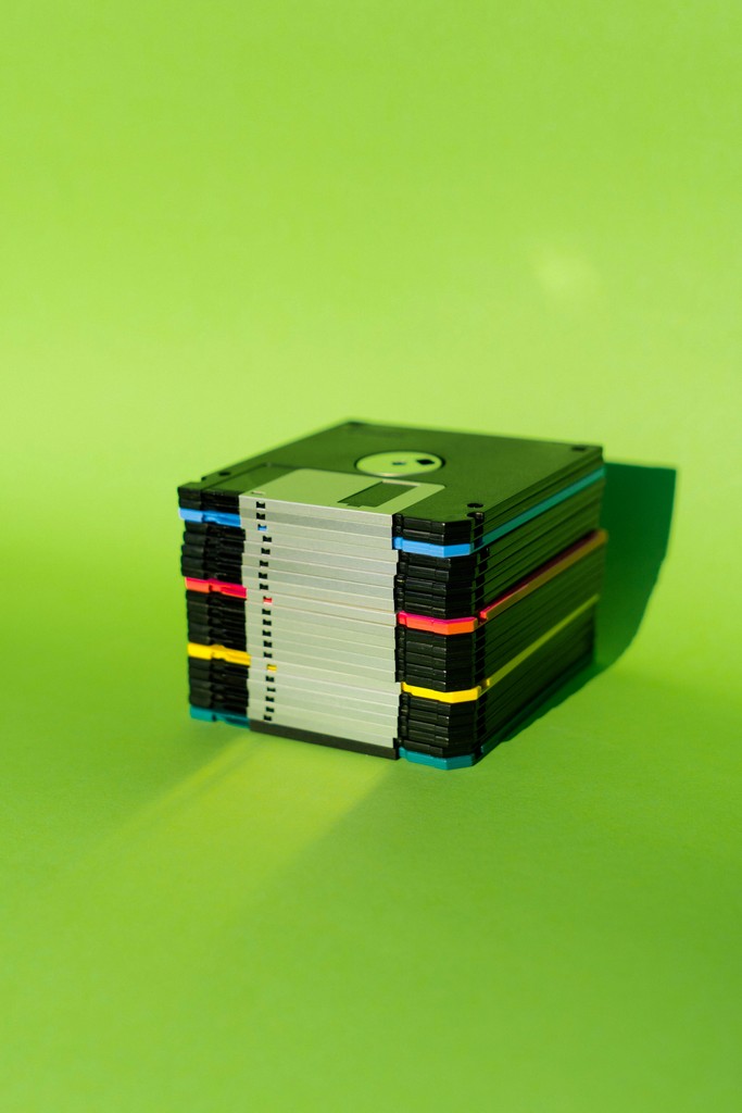  A neatly stacked pile of colorful floppy disks against a vibrant green background, representing vintage data storage and evoking a sense of technological nostalgia.